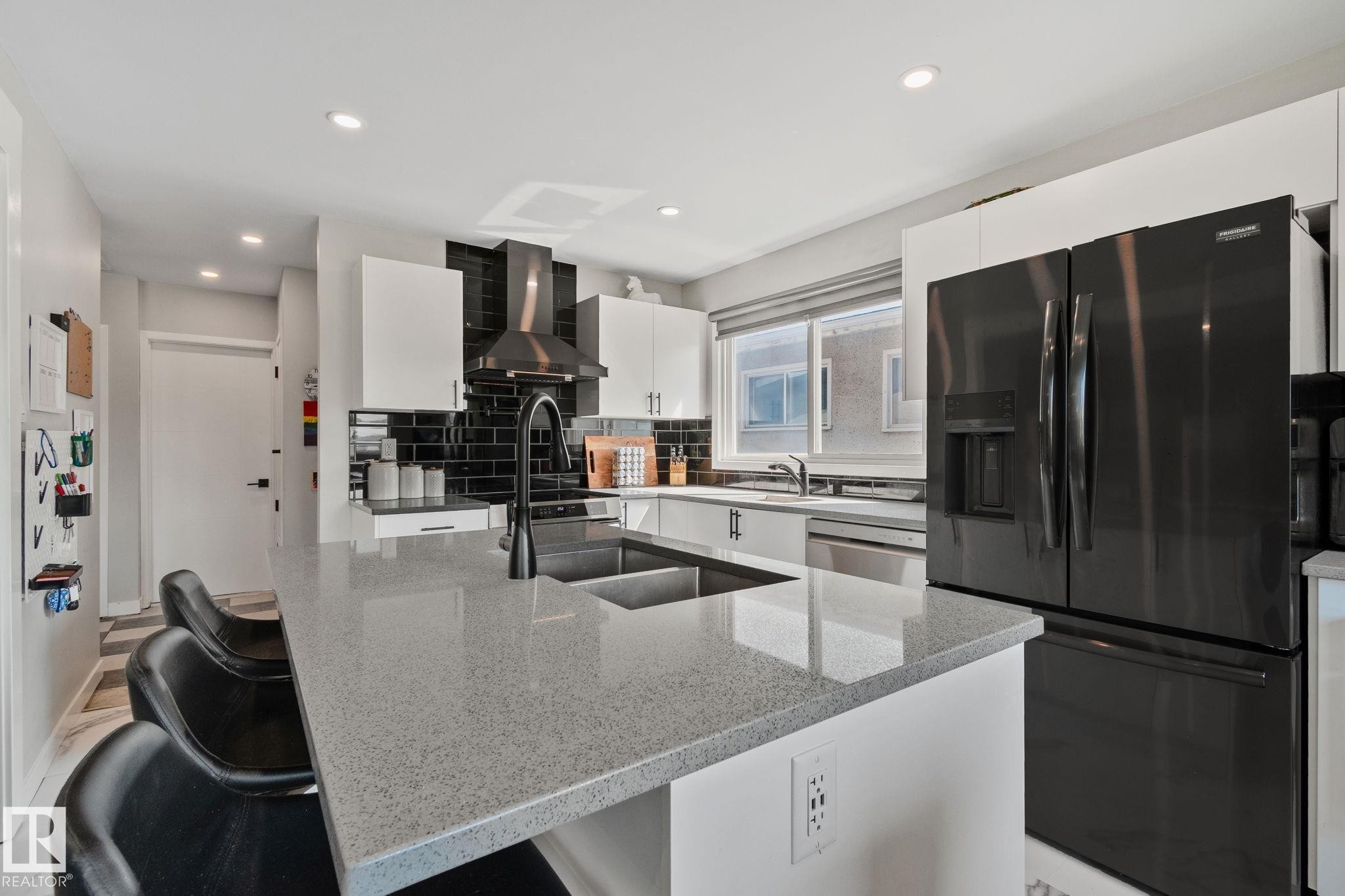 Kitchen featuring a large island with an undermount sink, light-toned countertop, and matte black faucet - 4723 105 Street Nw, Edmonton, AB - Indoor Photo Showing Kitchen With Double Sink With Upgraded Kitchen