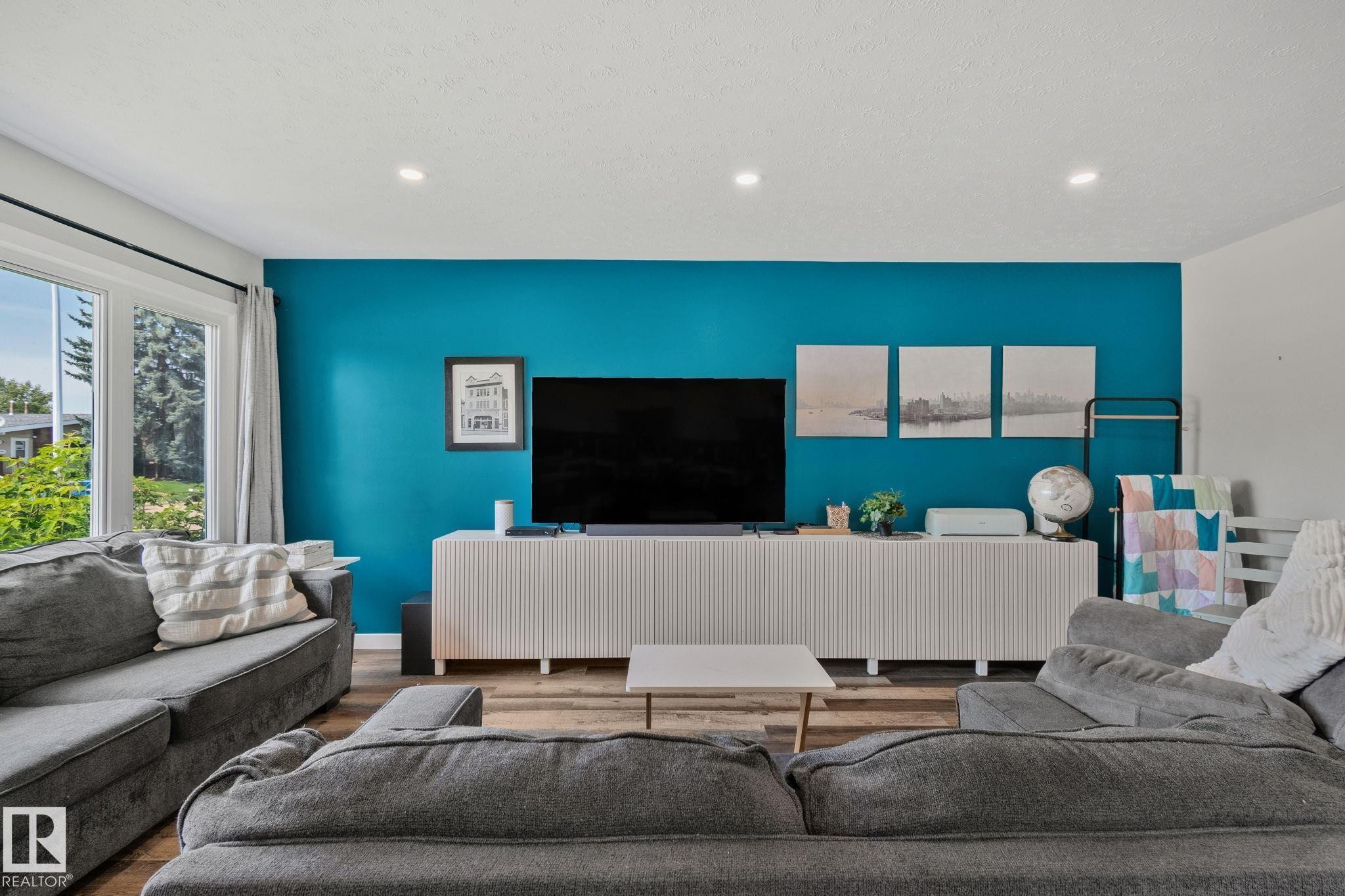 Open living area featuring a prominent accent wall and wood-finish flooring - 4723 105 Street Nw, Edmonton, AB - Indoor Photo Showing Living Room