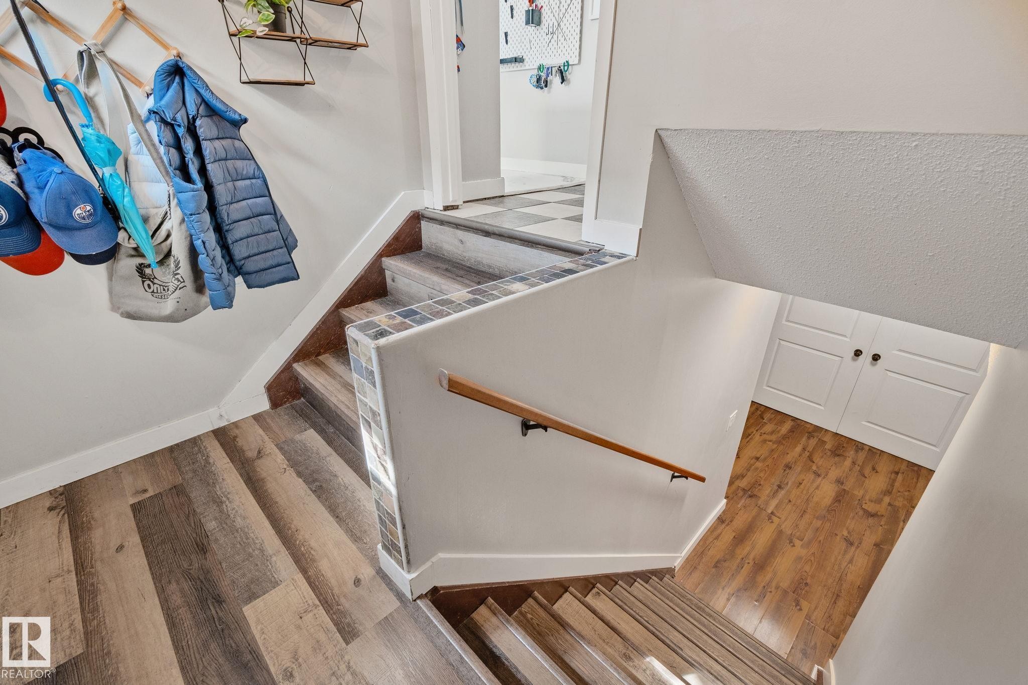 Multi-level interior featuring wood-finish flooring, a wood handrail, and built-in white paneled cabinetry - 4723 105 Street Nw, Edmonton, AB - Indoor Photo Showing Other Room