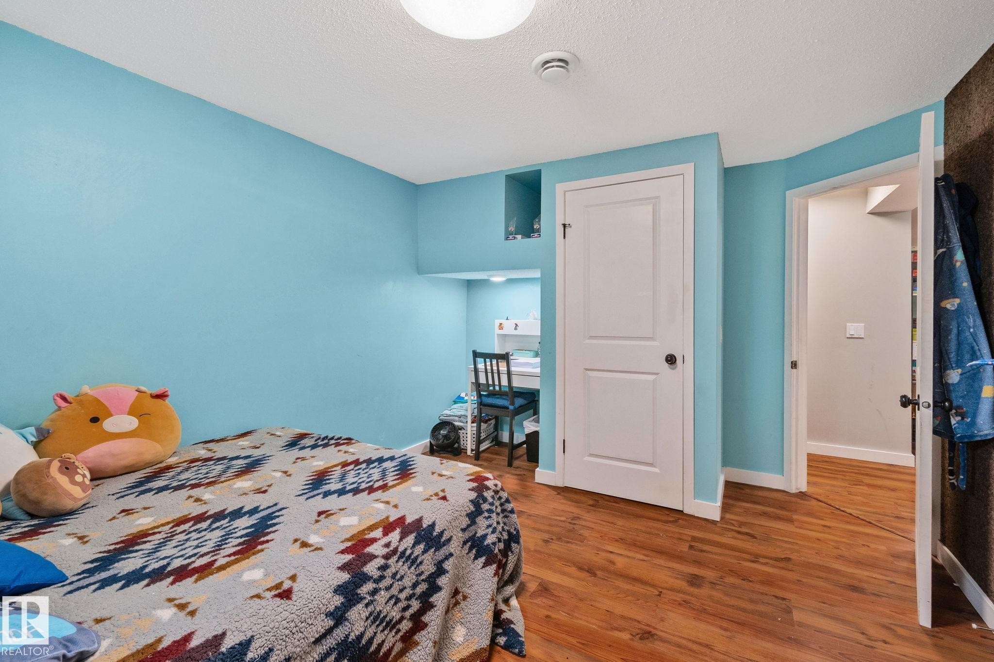 Room featuring wood-finish flooring, light blue walls, and a recessed desk area with built-in shelving - 4723 105 Street Nw, Edmonton, AB - Indoor Photo Showing Bedroom