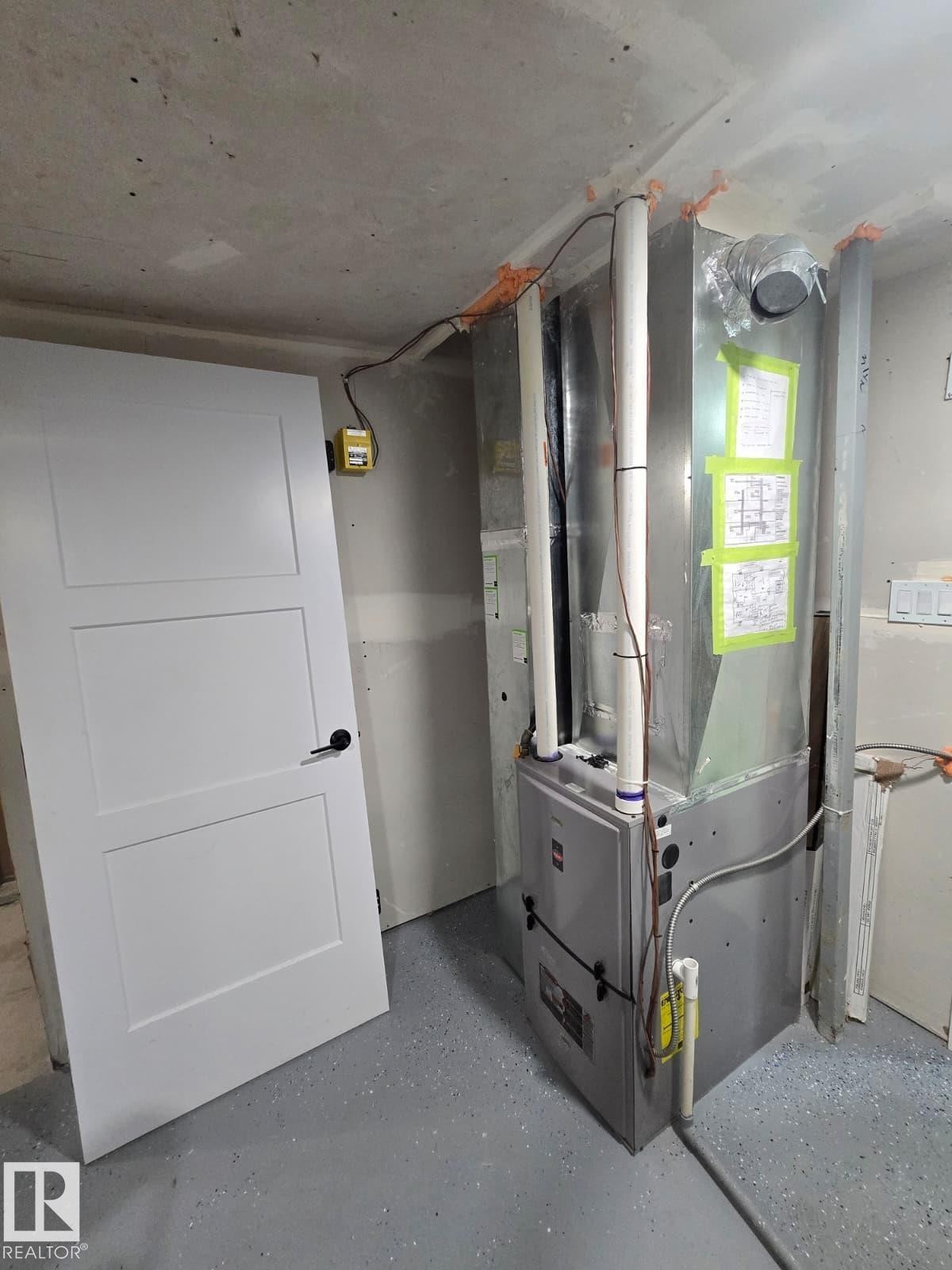 Modern HVAC system with exposed ductwork, concrete flooring, and a white three-panel door - 228 36 Street Sw, Edmonton, AB - Indoor Photo Showing Other Room