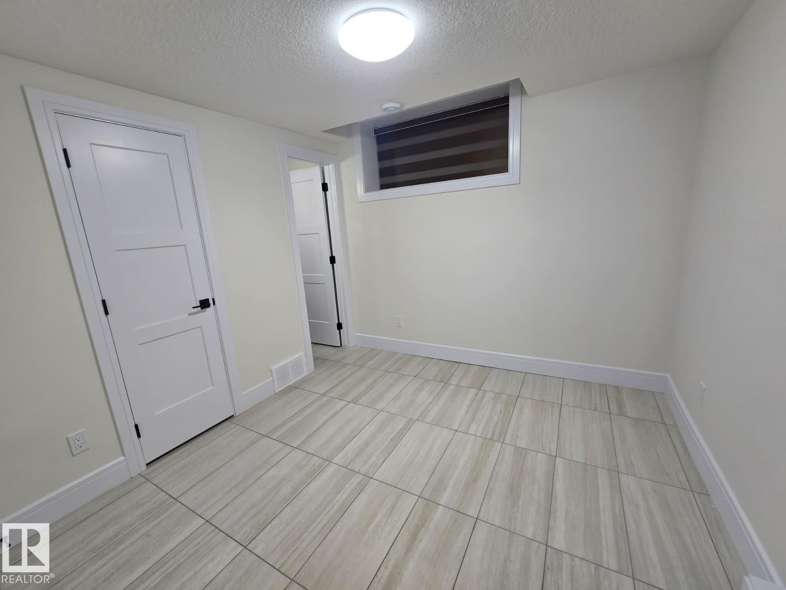 Neutral tone wall finishes, contemporary three-panel interior doors with black hardware, and an overhead flush-mount light fixture - 228 36 Street Sw, Edmonton, AB - Indoor Photo Showing Other Room