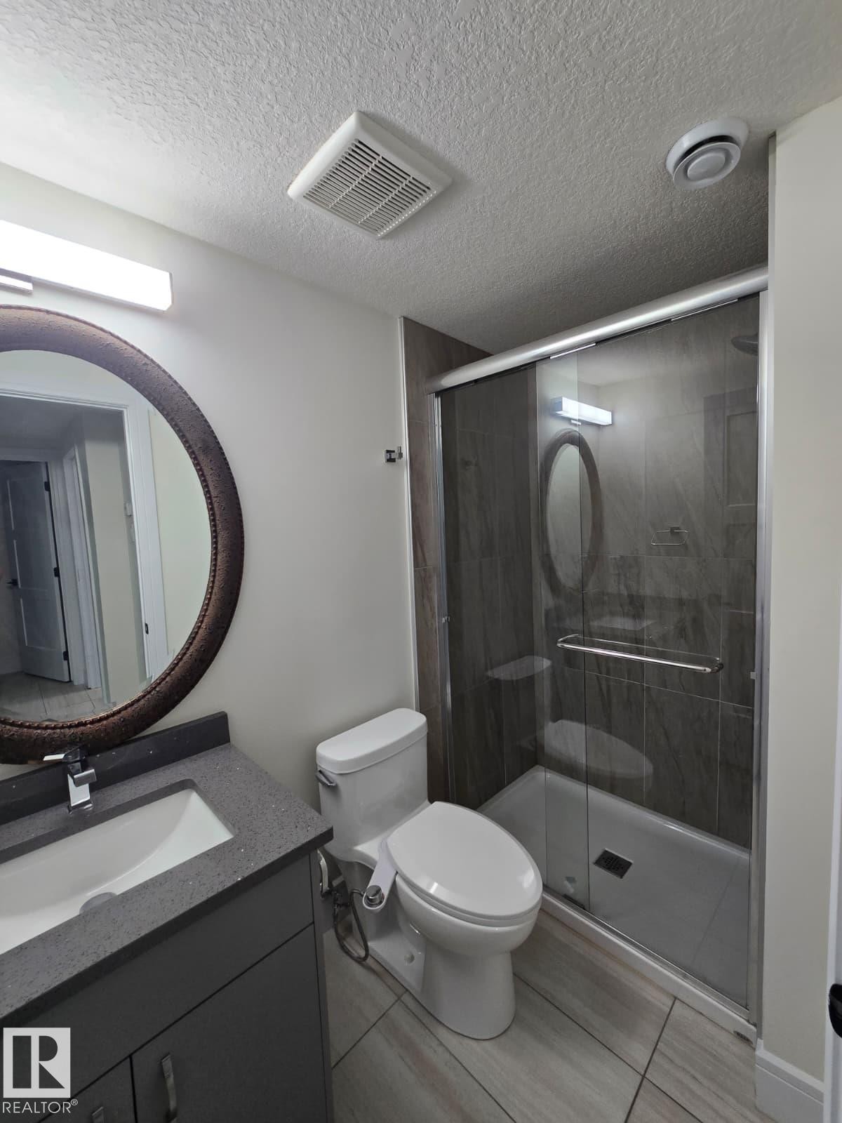 Modern bathroom featuring a sleek vanity with integrated sink and ample counter space, a contemporary toilet, and a walk-in shower enclosure with dark tile surround - 228 36 Street Sw, Edmonton, AB - Indoor Photo Showing Bathroom