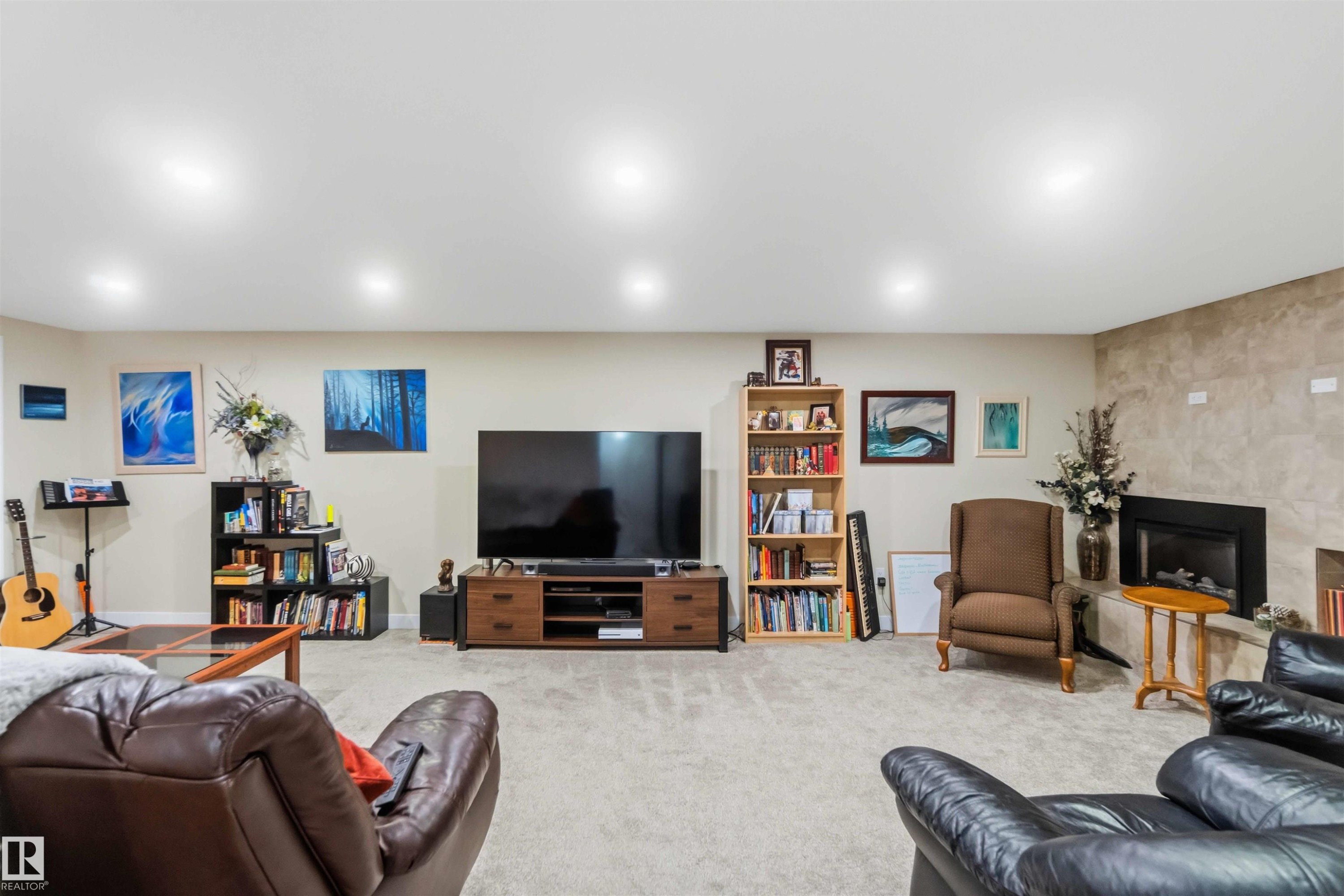 Spacious entertainment room featuring recessed lighting, light-toned carpeting, a built-in fireplace with a stone-finish surround, and neutral wall tones - 11351 35A Avenue Nw, Edmonton, AB - Indoor Photo Showing Basement
