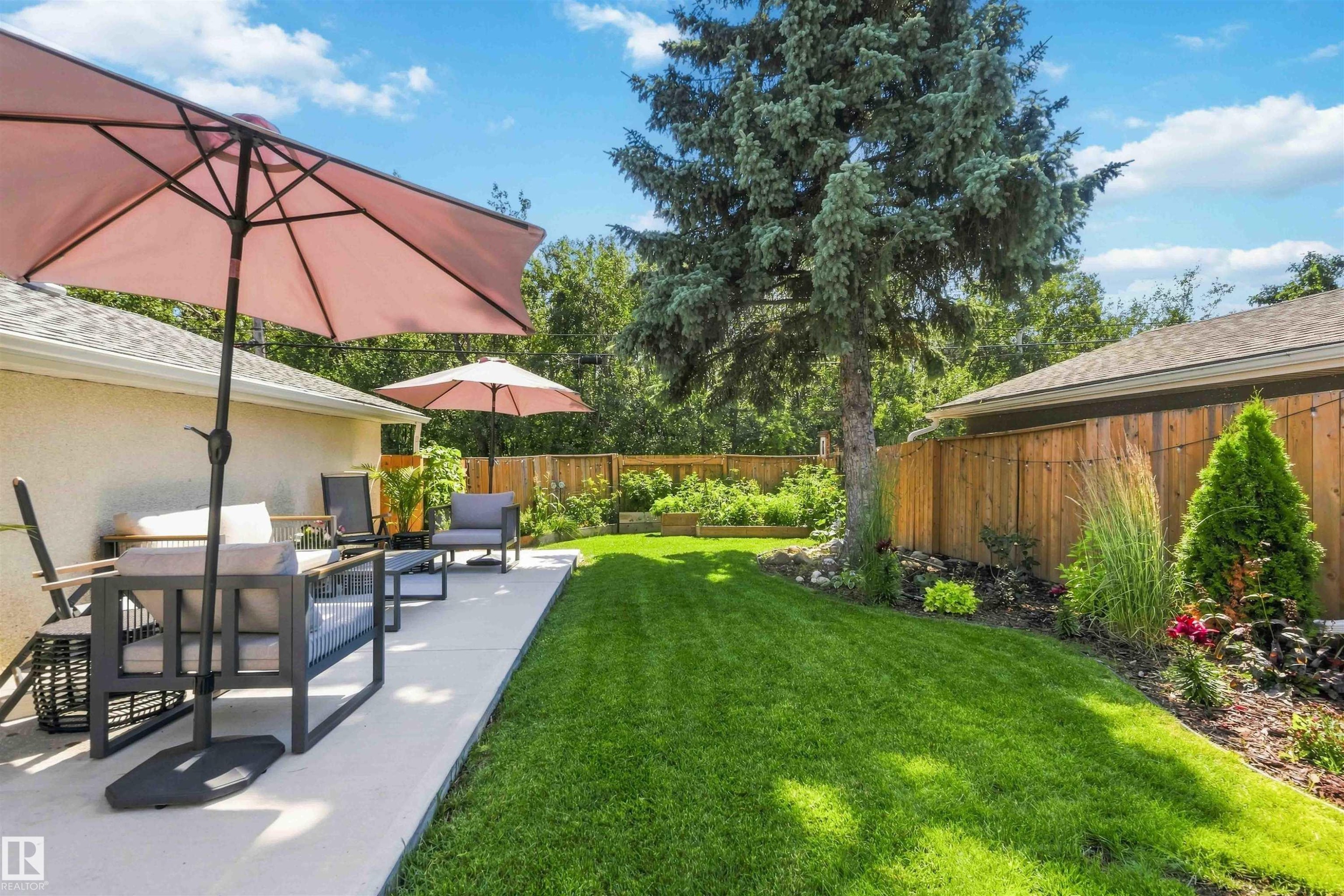 Expansive backyard featuring a concrete patio, lush green lawn, mature trees, and a wooden privacy fence - 11351 35A Avenue Nw, Edmonton, AB - Outdoor With Deck Patio Veranda