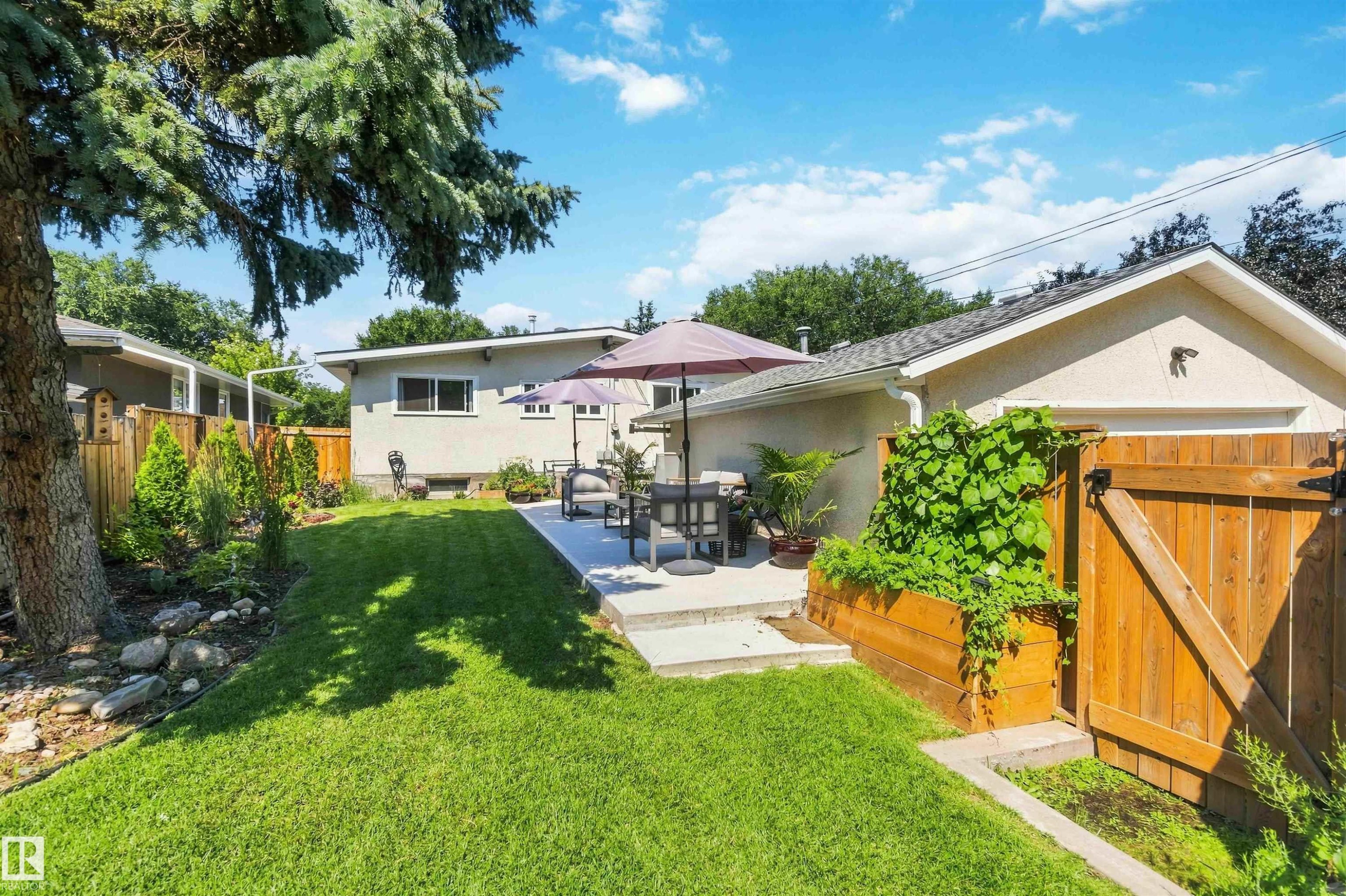 Spacious backyard featuring a manicured lawn, a concrete patio, a wooden privacy fence, a raised garden bed, and mature trees - 11351 35A Avenue Nw, Edmonton, AB - Outdoor With Deck Patio Veranda