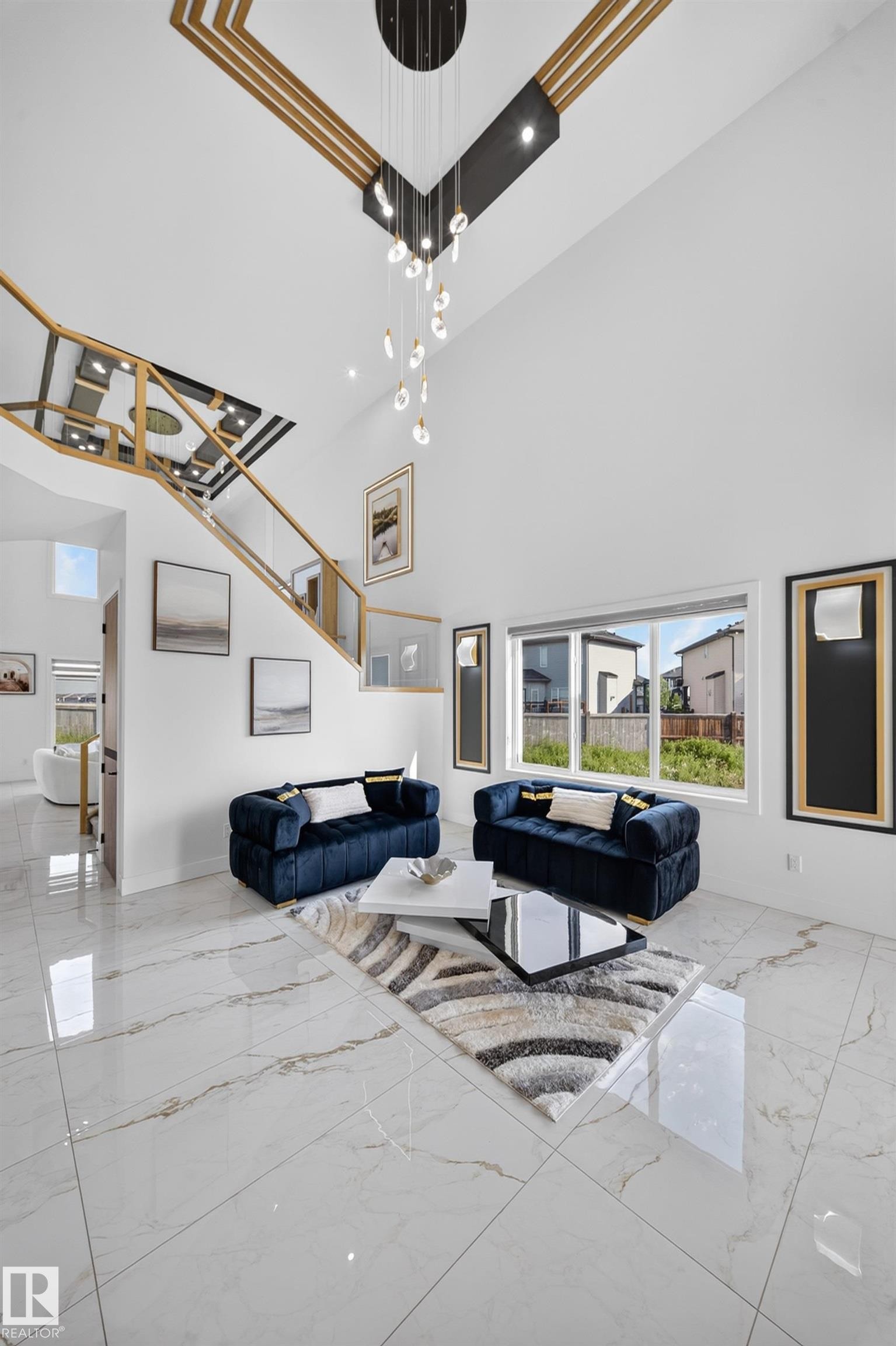 Spacious living area featuring double-height ceilings, a contemporary chandelier, large format porcelain tile flooring, and a sophisticated open-tread staircase with glass railing - 423 Robinson Bv, Leduc, AB - Indoor Photo Showing Other Room