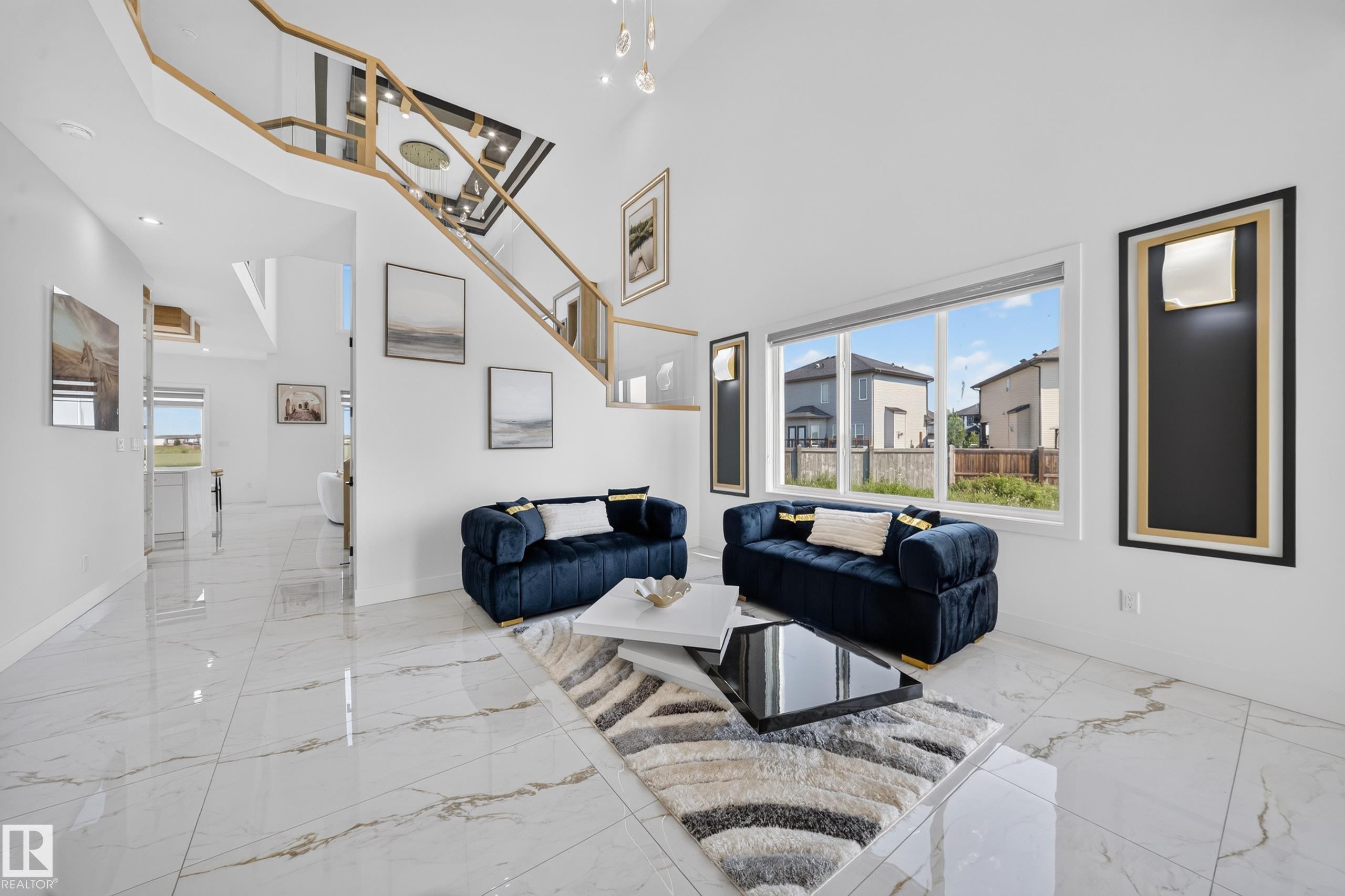 Bright open-concept living area featuring a double-height ceiling, large picture windows, and a contemporary open-riser staircase with a gold-tone railing - 423 Robinson Bv, Leduc, AB - Indoor