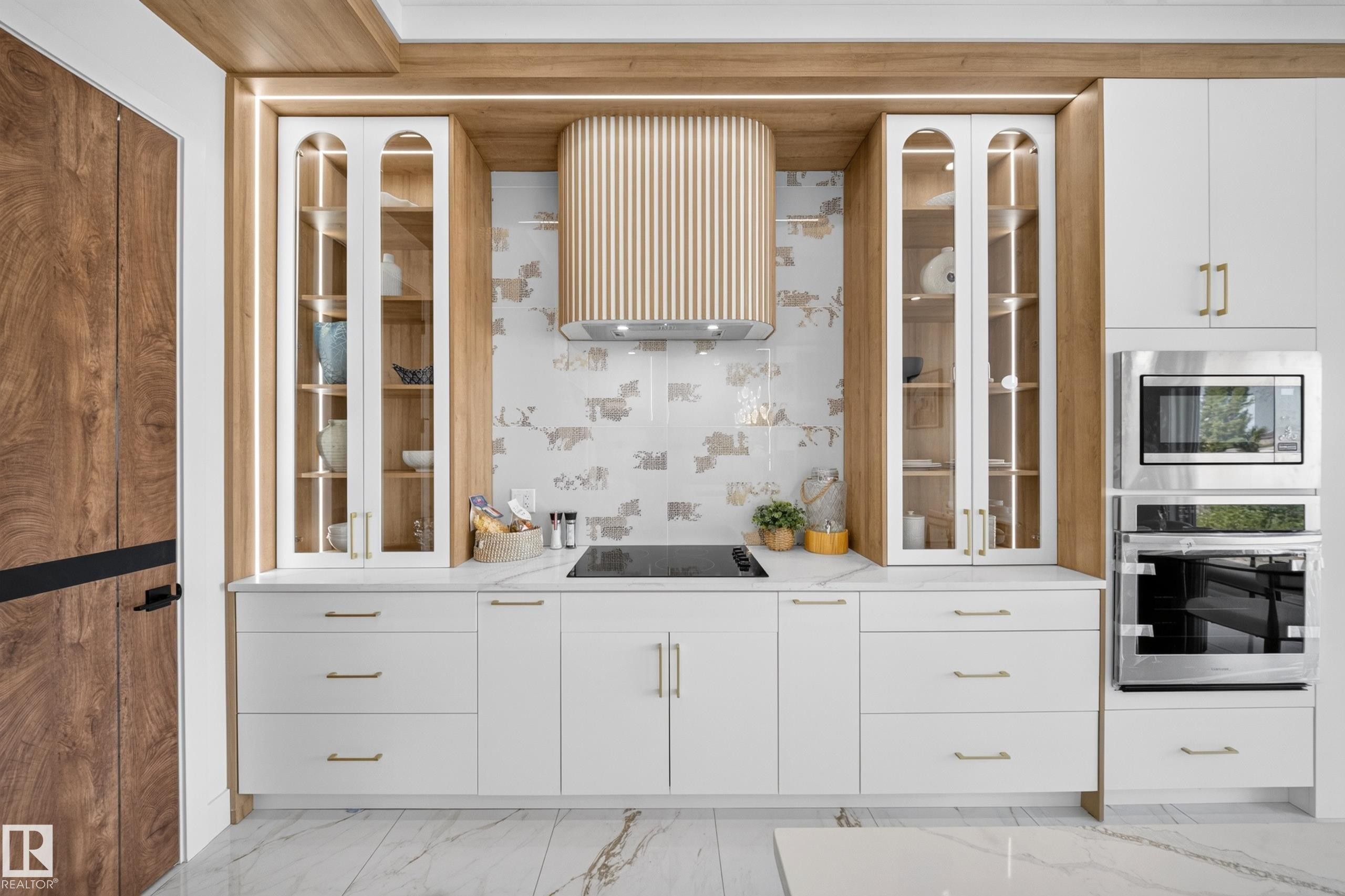 Modern kitchen featuring white cabinetry with gold-tone hardware, a sleek cooktop, and a custom wood-finish range hood - 423 Robinson Bv, Leduc, AB - Indoor Photo Showing Kitchen