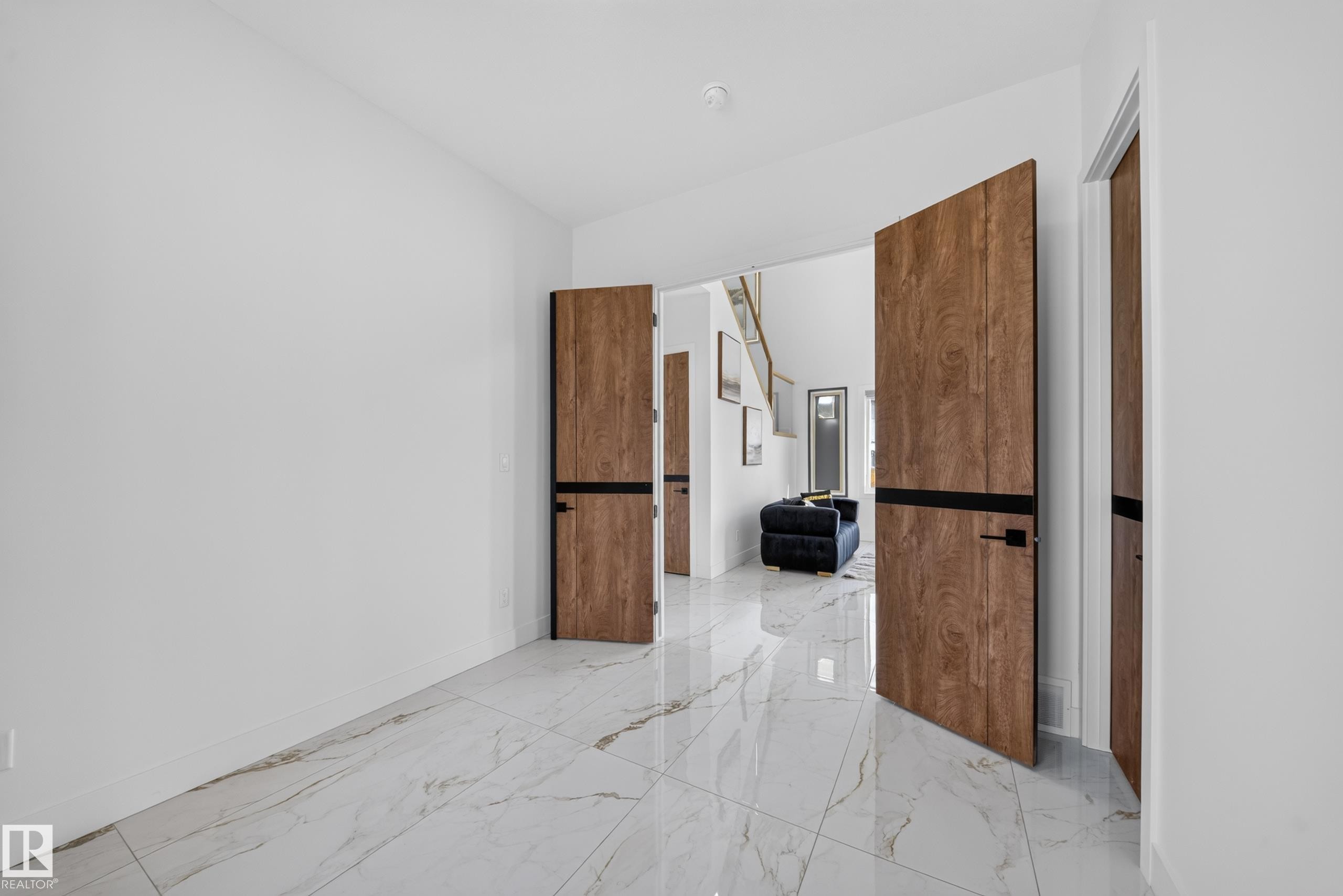 Entryway featuring large format white tile flooring with veining, solid wood-finish doors with black banding and hardware, and bright white walls - 423 Robinson Bv, Leduc, AB - Indoor