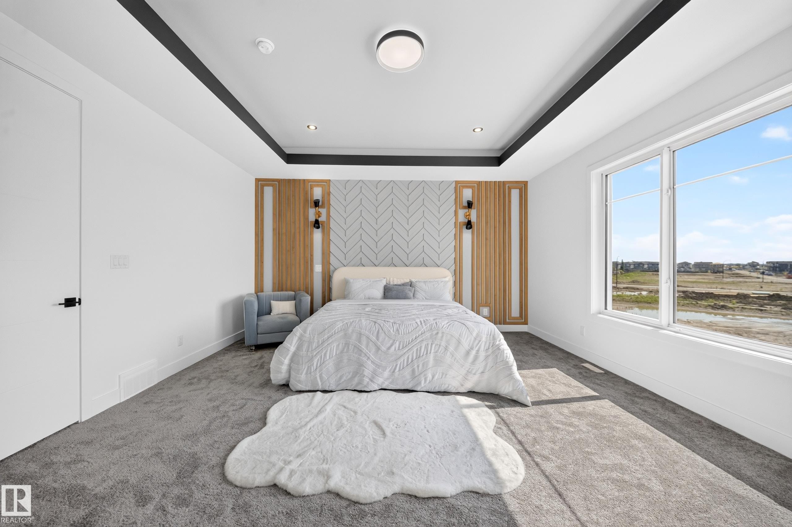 Spacious room featuring a tray ceiling with dark accent trim, wall-mounted sconces, and a large window - 423 Robinson Bv, Leduc, AB - Indoor Photo Showing Bedroom