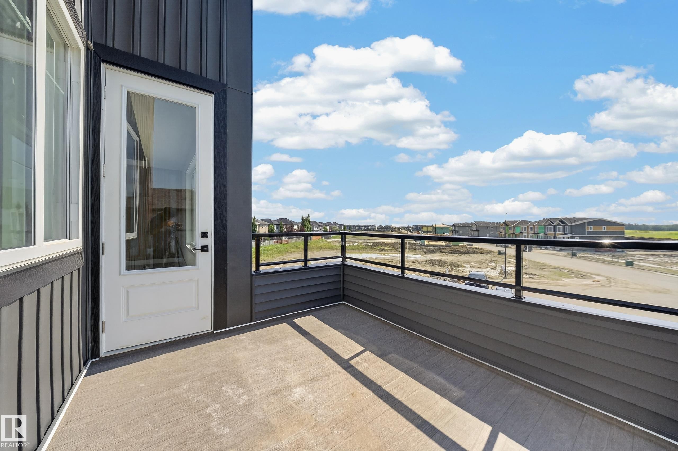 Exterior balcony featuring dark horizontal siding, a clear glass and metal railing, and a white glass-paneled door - 423 Robinson Bv, Leduc, AB - Outdoor With View