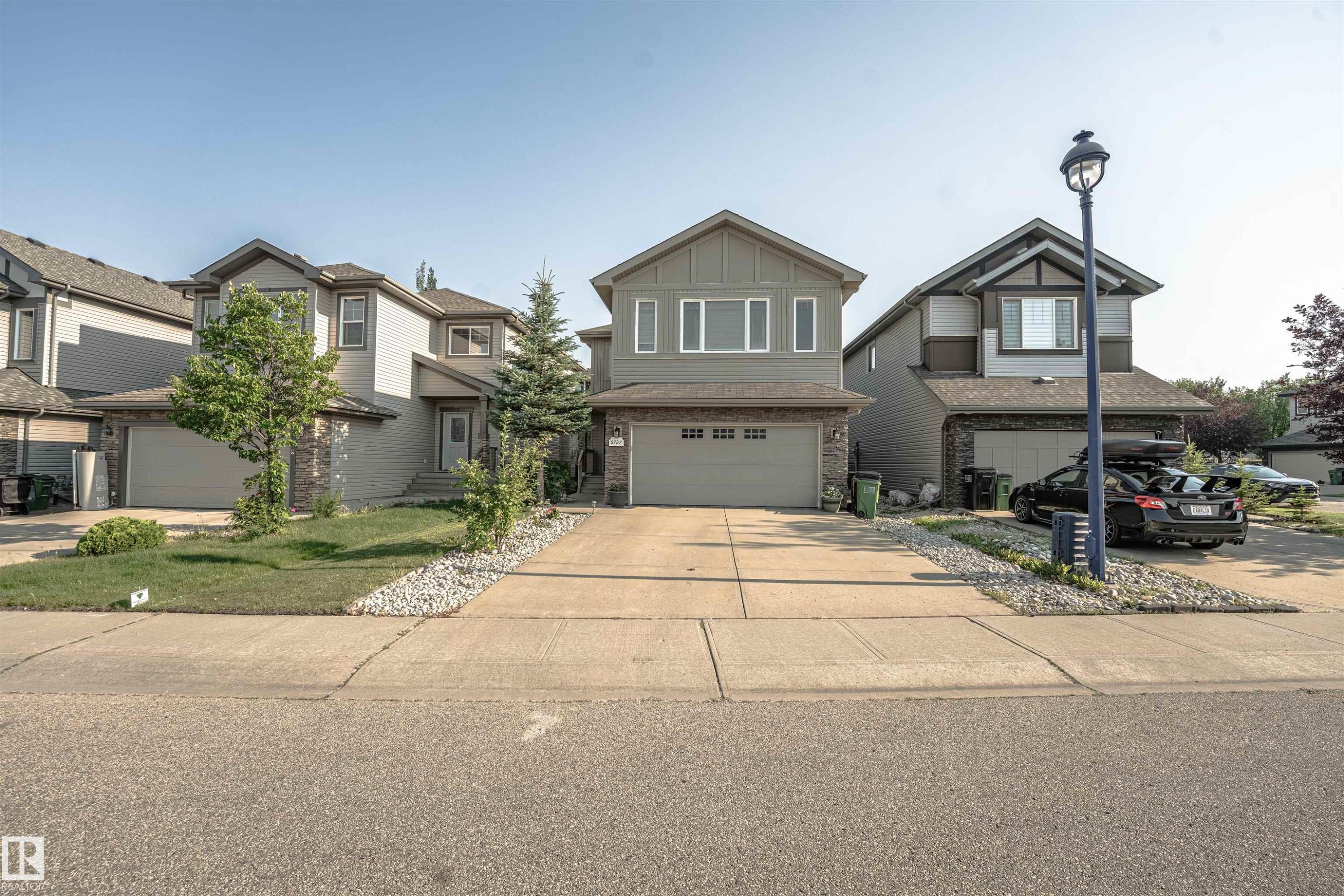 Two-story residential architecture featuring a gray siding exterior with stone accenting, a concrete driveway, and an integrated single-car garage - 6727 20 Ave Sw, Edmonton, AB - Outdoor With Facade