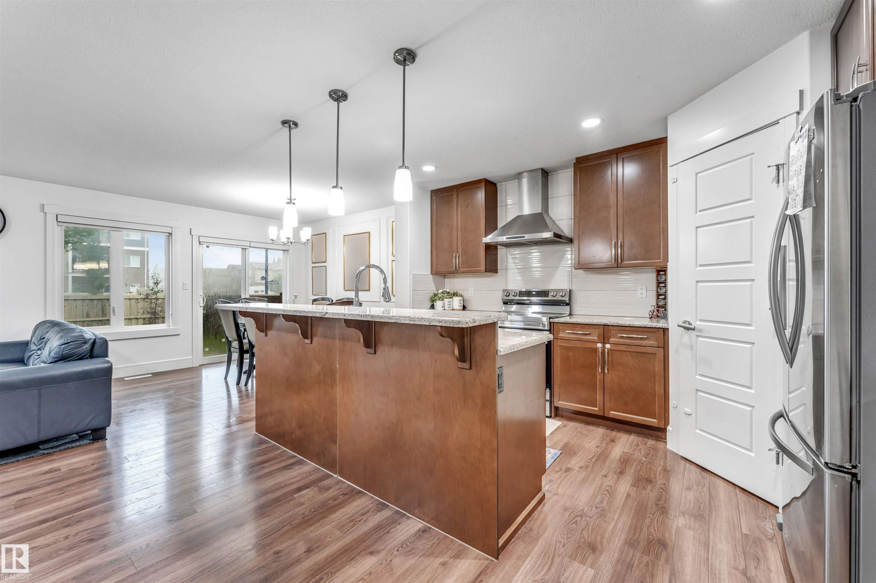 Open-concept kitchen featuring an island with a breakfast bar, recessed lighting, wood-finish flooring, and stainless steel appliances - 6727 20 Ave Sw, Edmonton, AB - Indoor Photo Showing Kitchen With Upgraded Kitchen
