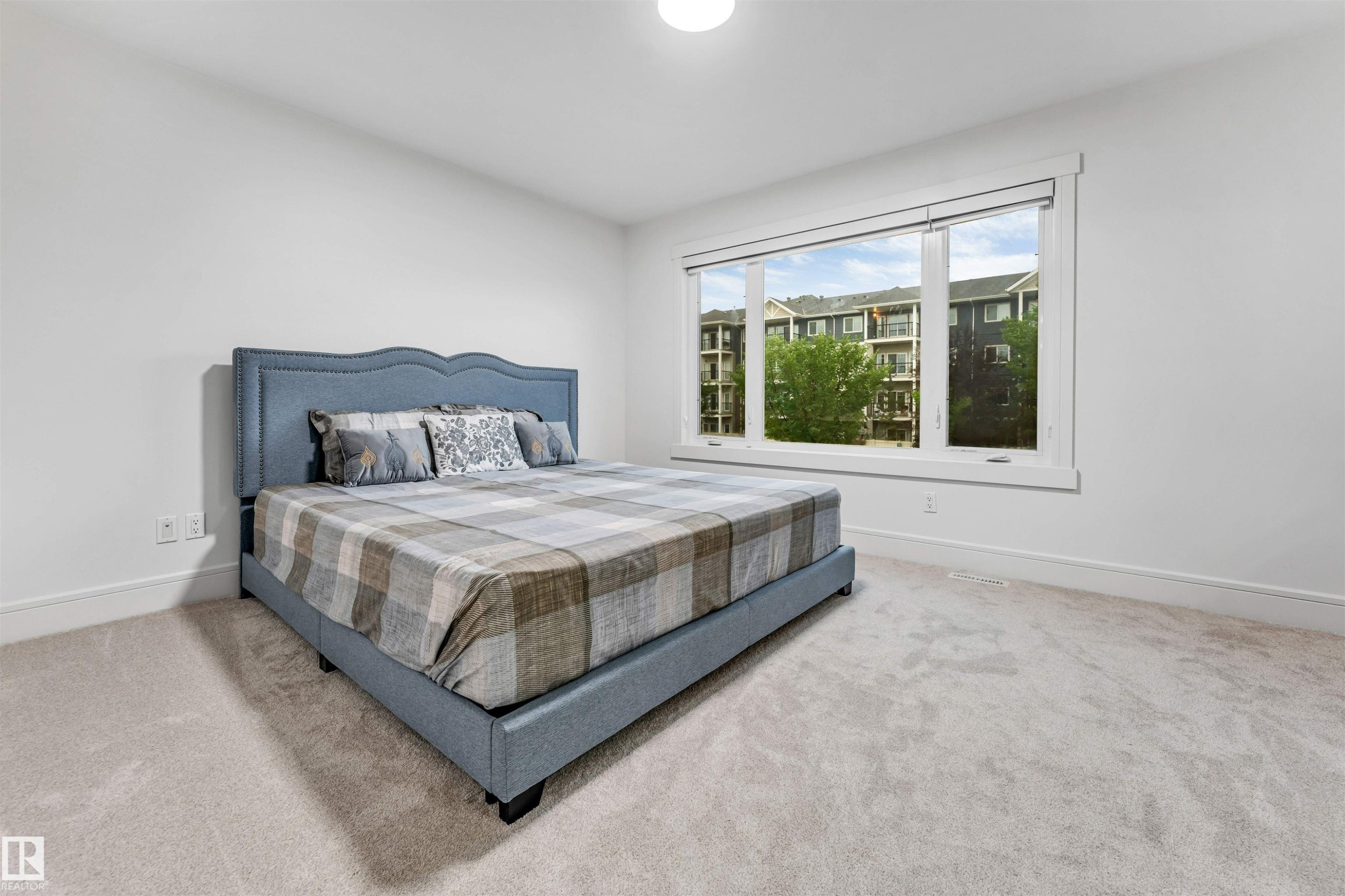 Bright bedroom featuring a large picture window, light-toned carpeting, white walls, and substantial white baseboards - 6727 20 Ave Sw, Edmonton, AB - Indoor Photo Showing Bedroom