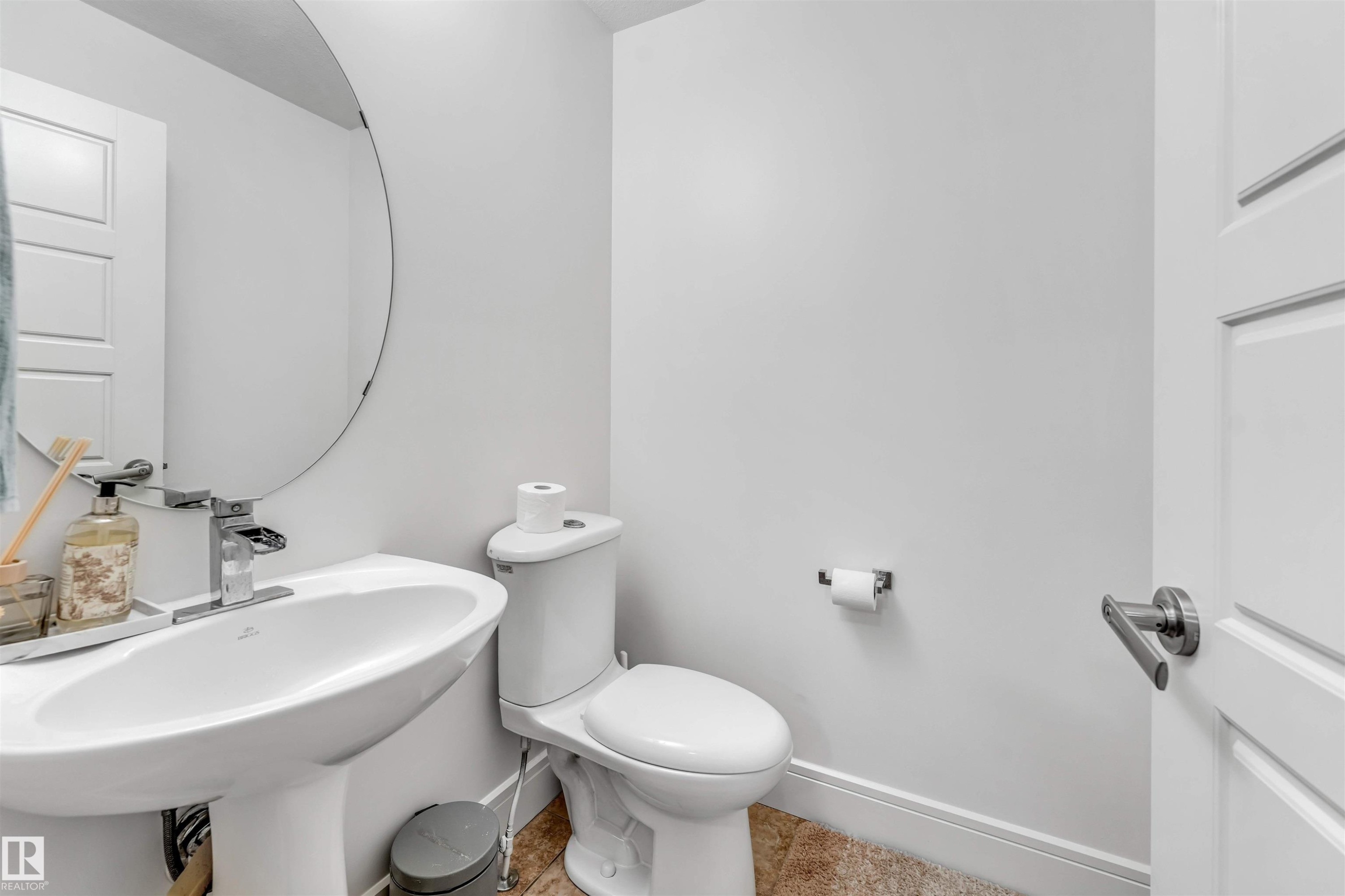 Pedestal sink with chrome faucet, circular mirror, and white paneled door - 6727 20 Ave Sw, Edmonton, AB - Indoor Photo Showing Bathroom