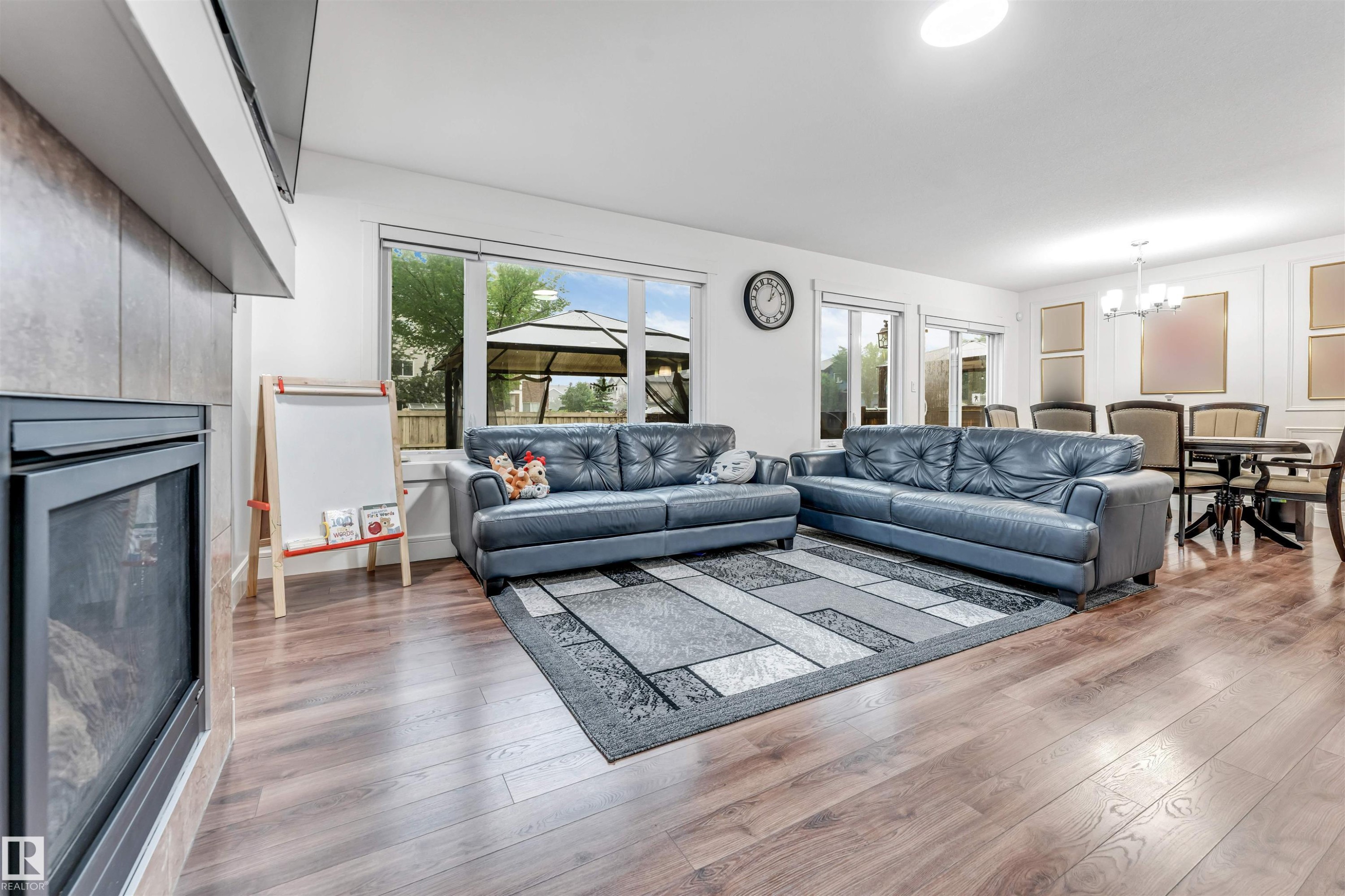 Open-concept living area featuring wood-finish flooring, a tiled fireplace surround, and multiple windows - 6727 20 Ave Sw, Edmonton, AB - Indoor Photo Showing Living Room With Fireplace