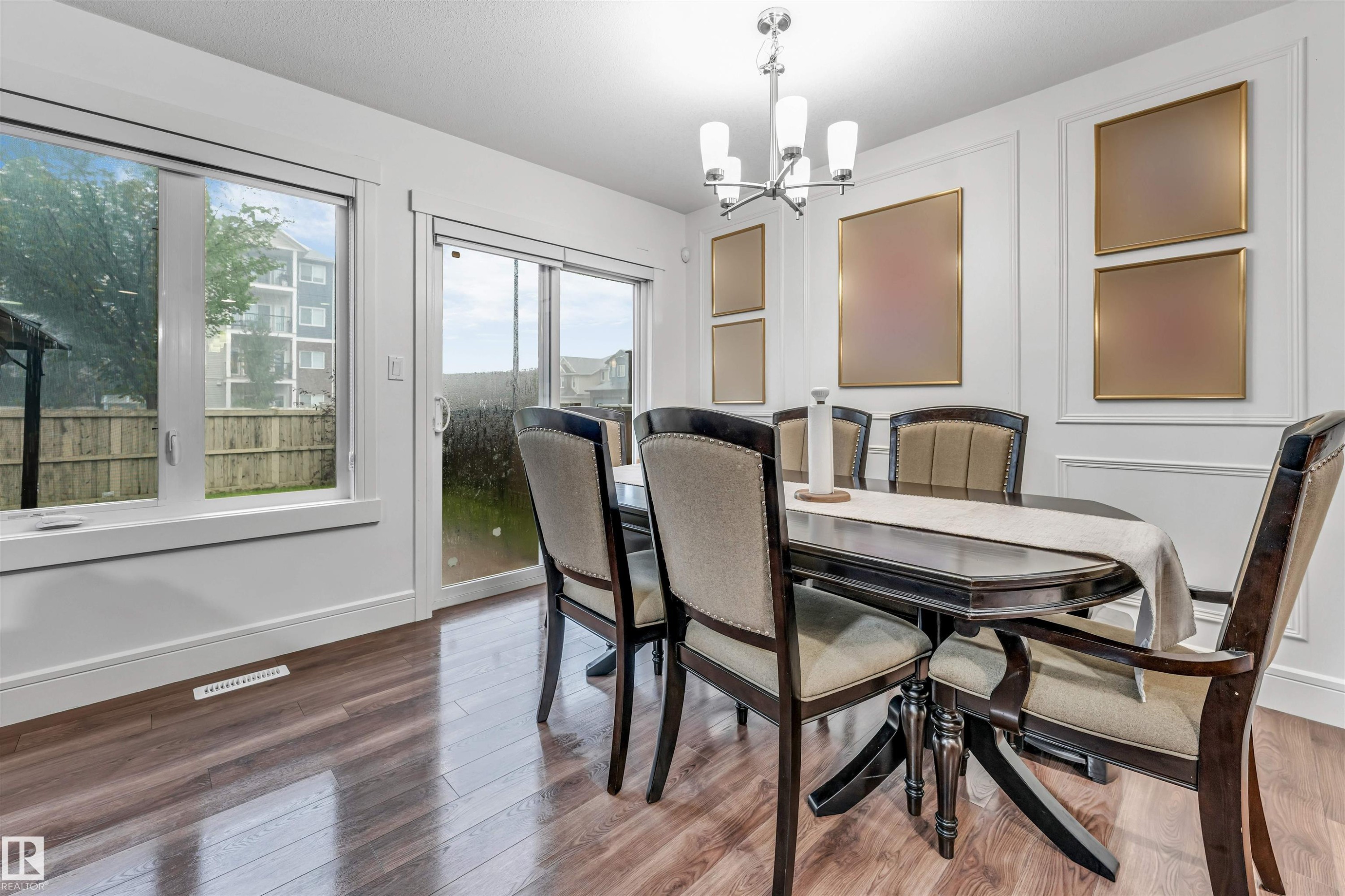 Open-concept dining area featuring wood-finish flooring, a contemporary chandelier, large picture window, and sliding glass door - 6727 20 Ave Sw, Edmonton, AB - Indoor Photo Showing Dining Room