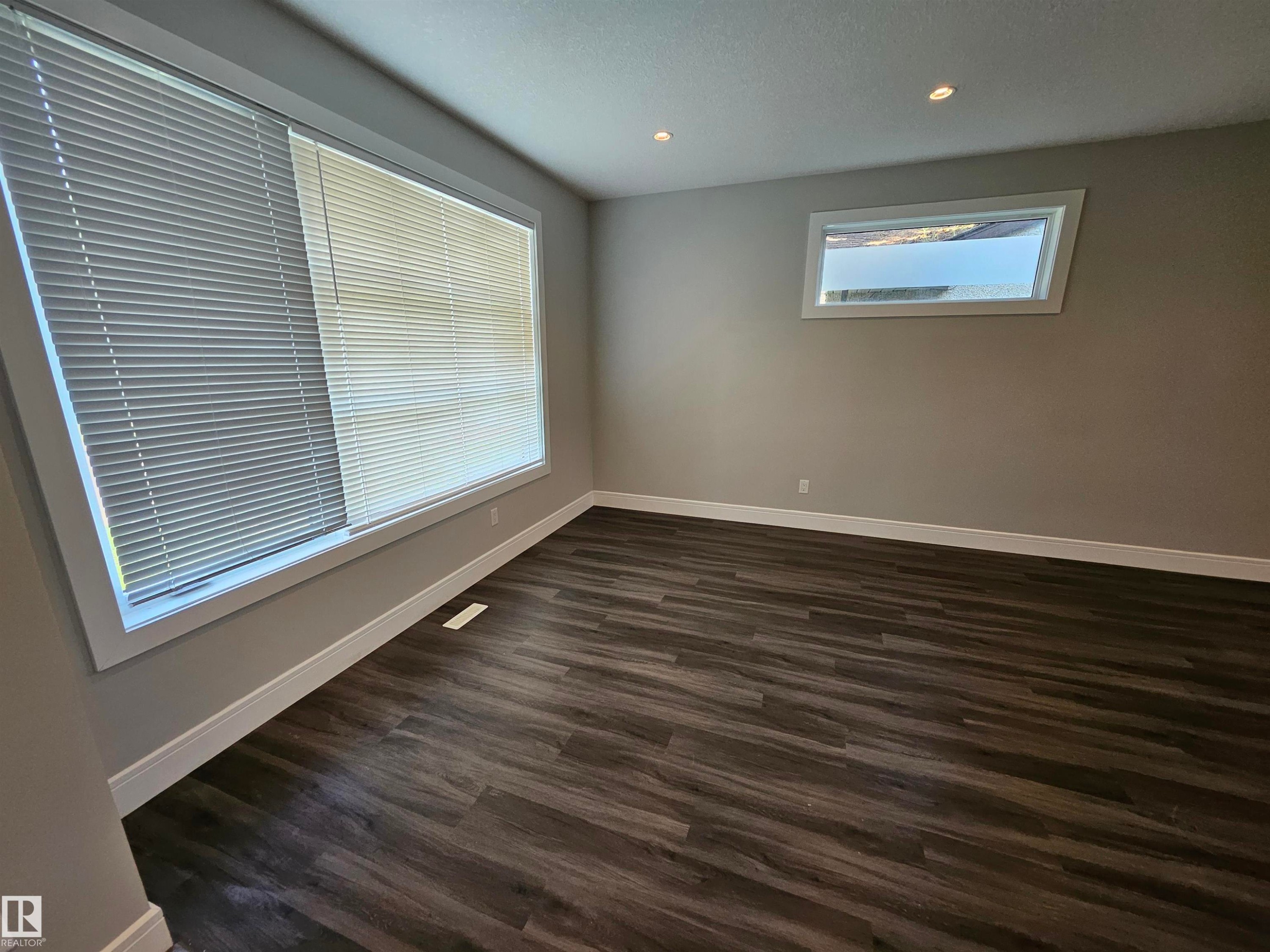 Spacious room featuring wood-finish flooring, two large windows with blinds, recessed ceiling lighting, and neutral wall paint - 9311 66 Avenue Nw, Edmonton, AB - Indoor Photo Showing Other Room