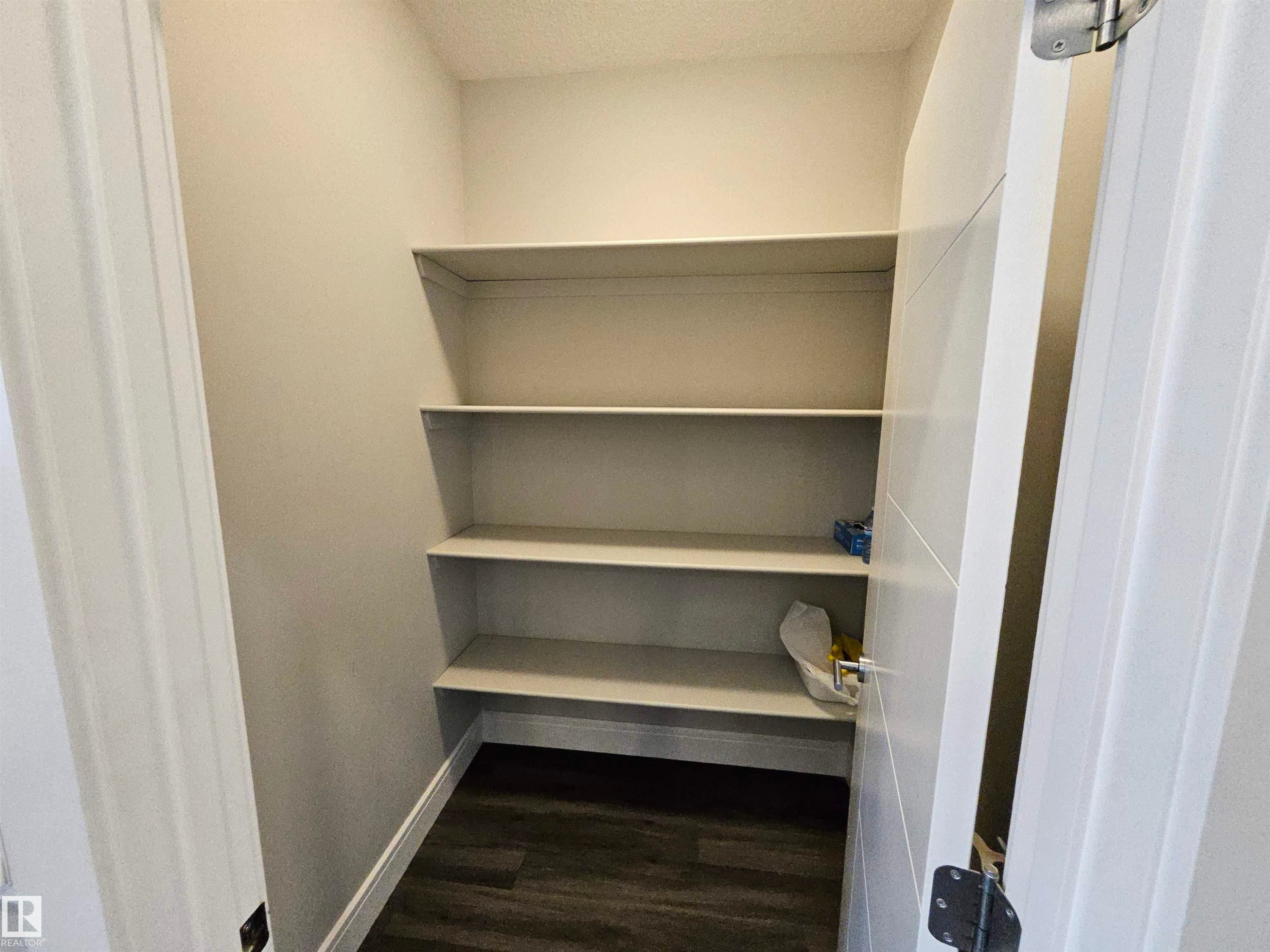 Pantry featuring multiple built-in shelving units, light-toned walls, and wood-finish flooring - 9311 66 Avenue Nw, Edmonton, AB - Indoor With Storage