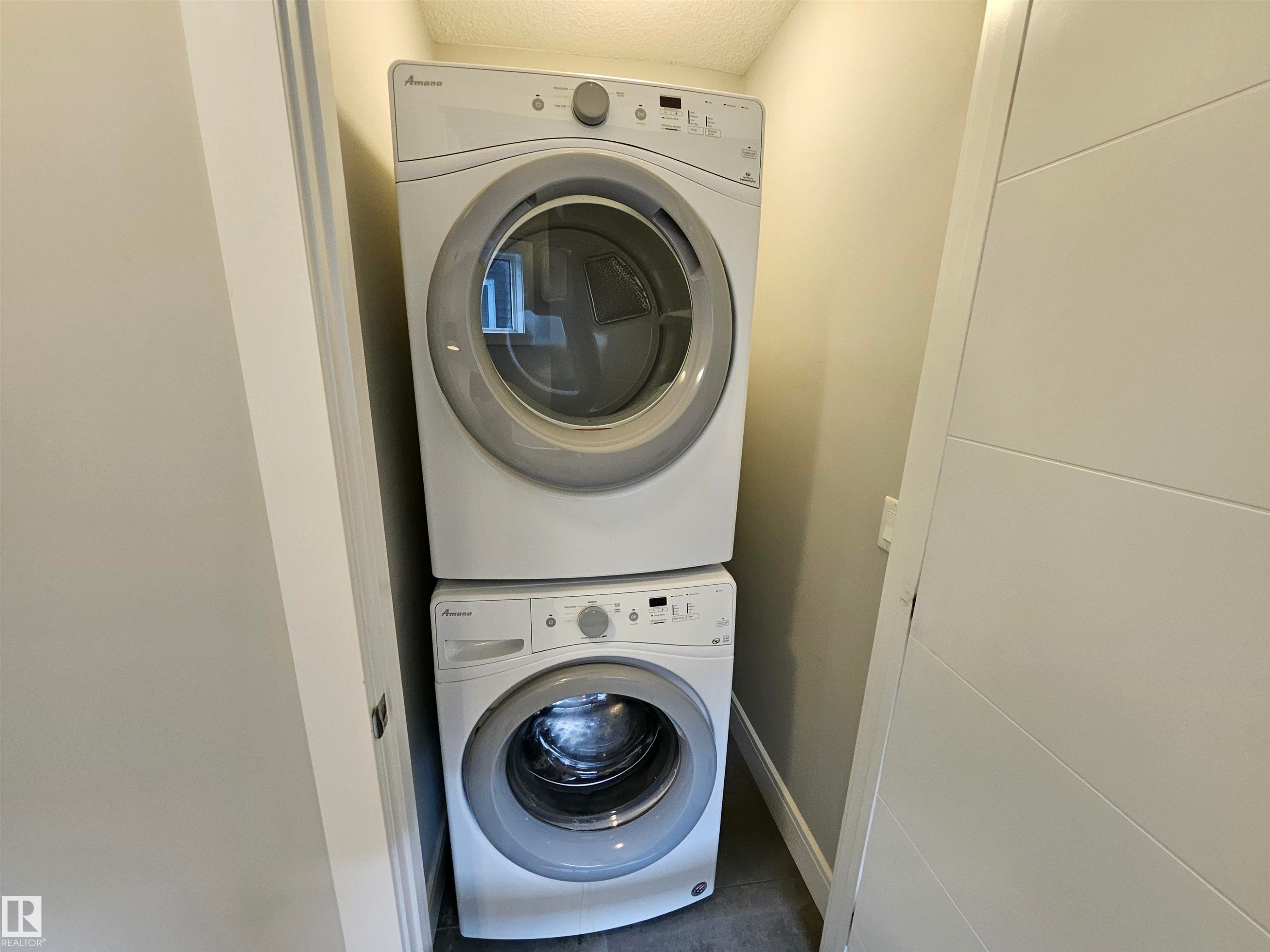 Stackable white washer and dryer units within a dedicated laundry alcove, featuring a paneled door - 9311 66 Avenue Nw, Edmonton, AB - Indoor Photo Showing Laundry Room