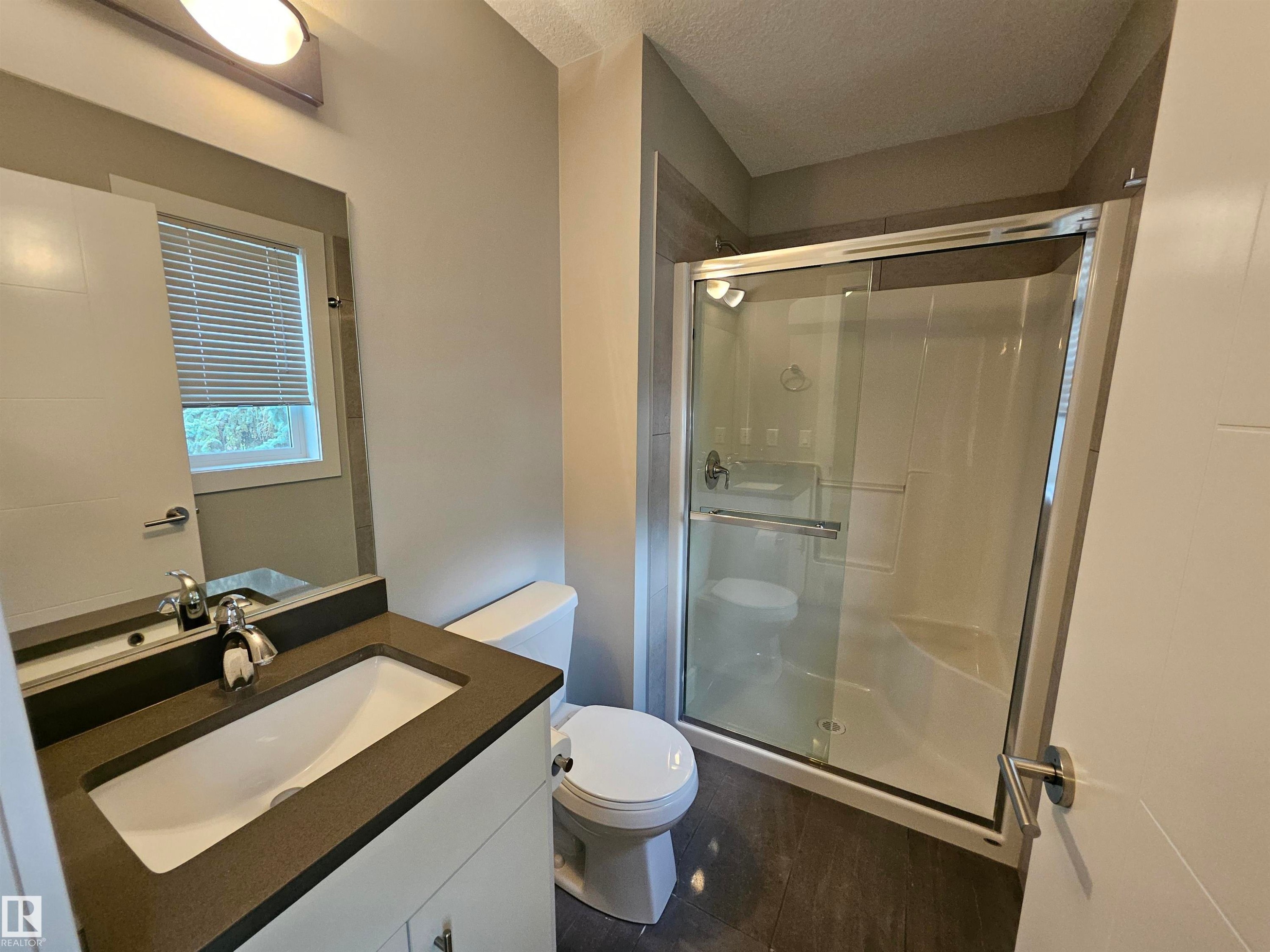 Contemporary bathroom featuring a dark wood-finish flooring, a white vanity with a dark countertop, an undermount sink, and a glass-enclosed shower with tiled walls - 9311 66 Avenue Nw, Edmonton, AB - Indoor Photo Showing Bathroom