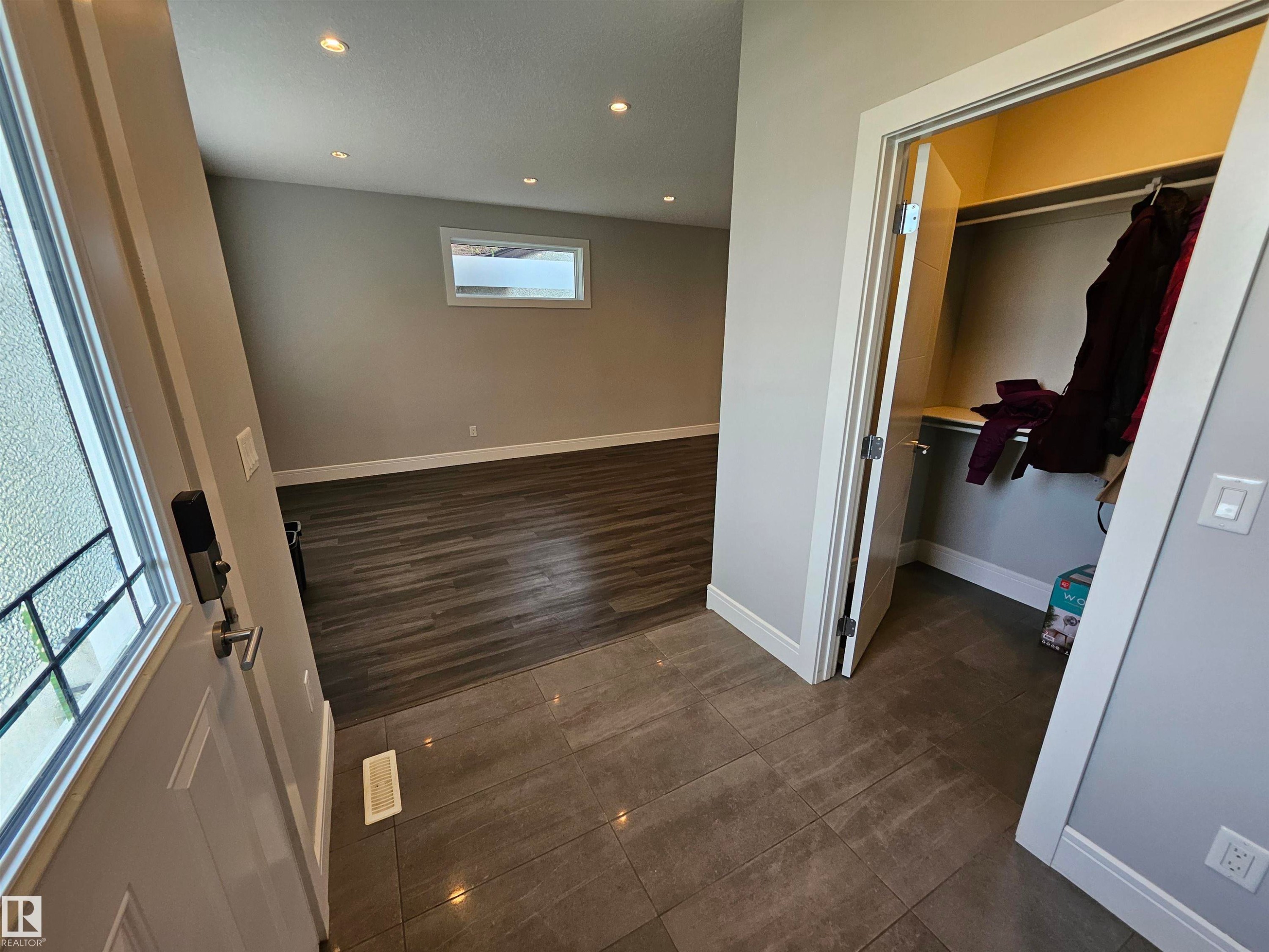 Tiled entry with a built-in closet featuring shelving and a hanging rod, leading to a room with wood-finish flooring, a rectangular window, and recessed lighting - 9311 66 Avenue Nw, Edmonton, AB - Indoor Photo Showing Other Room