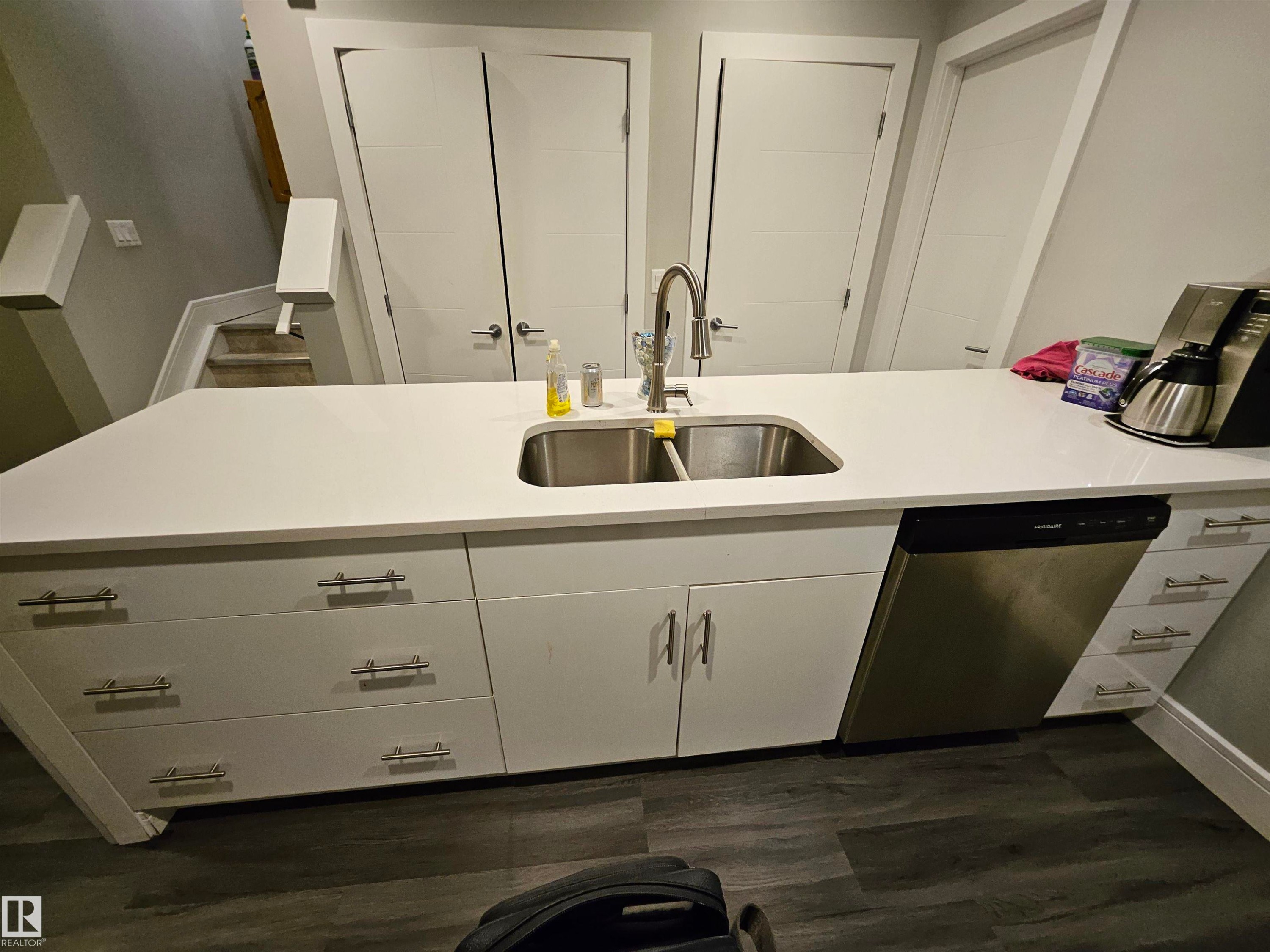 Contemporary kitchen island featuring a white countertop with an undermount double-basin stainless steel sink and a pull-down faucet - 9311 66 Avenue Nw, Edmonton, AB - Indoor Photo Showing Kitchen With Double Sink