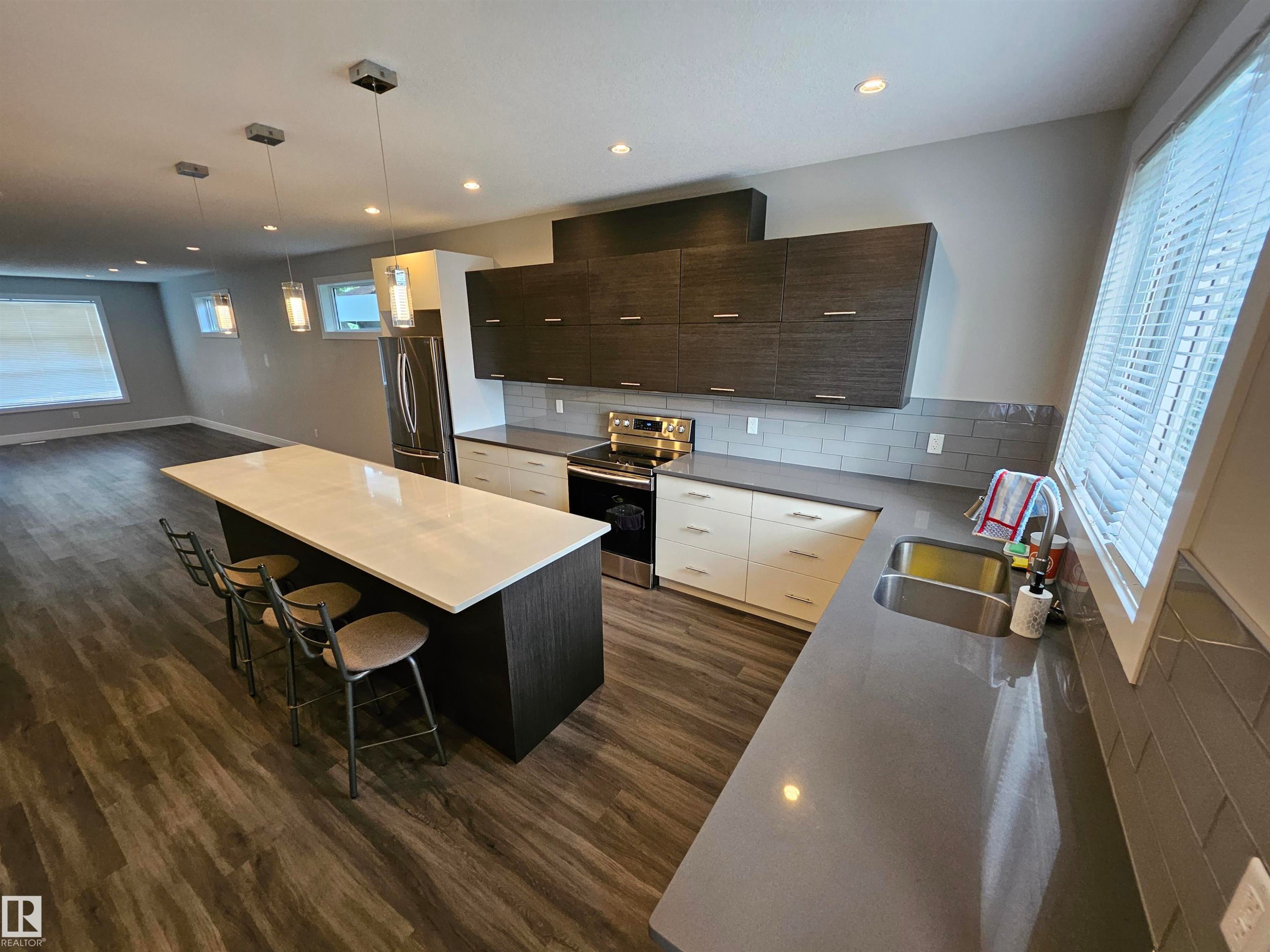 Open-concept kitchen featuring an oversized island with a white surface, contrasting dark wood-finish cabinetry, stainless steel appliances, grey subway tile backsplash, and recessed lighting - 9311 66 Avenue Nw, Edmonton, AB - Indoor Photo Showing Kitchen With Double Sink With Upgraded Kitchen