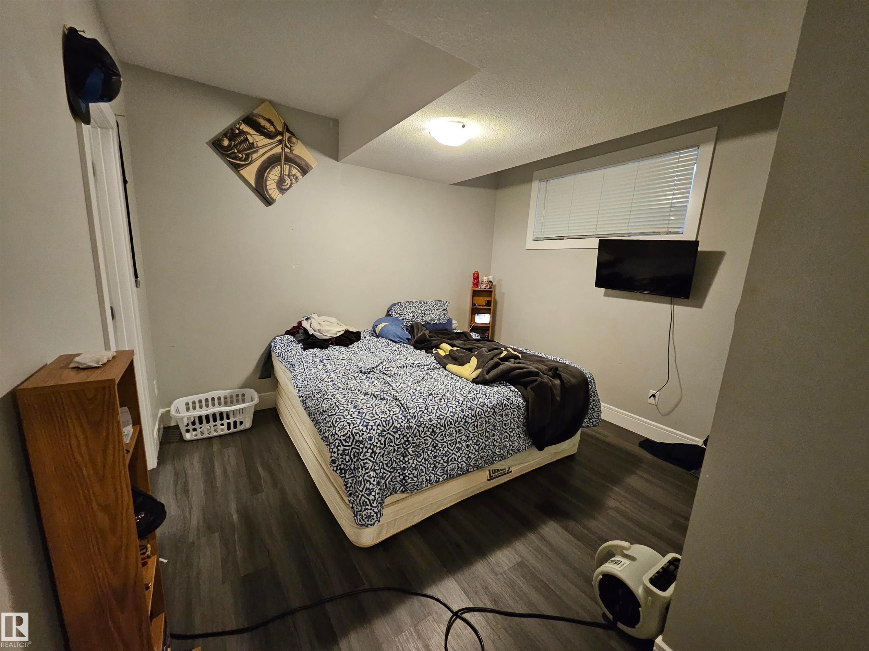 Room featuring wood-finish flooring, a wall-mounted television, and a window with blinds - 9311 66 Avenue Nw, Edmonton, AB - Indoor Photo Showing Bedroom