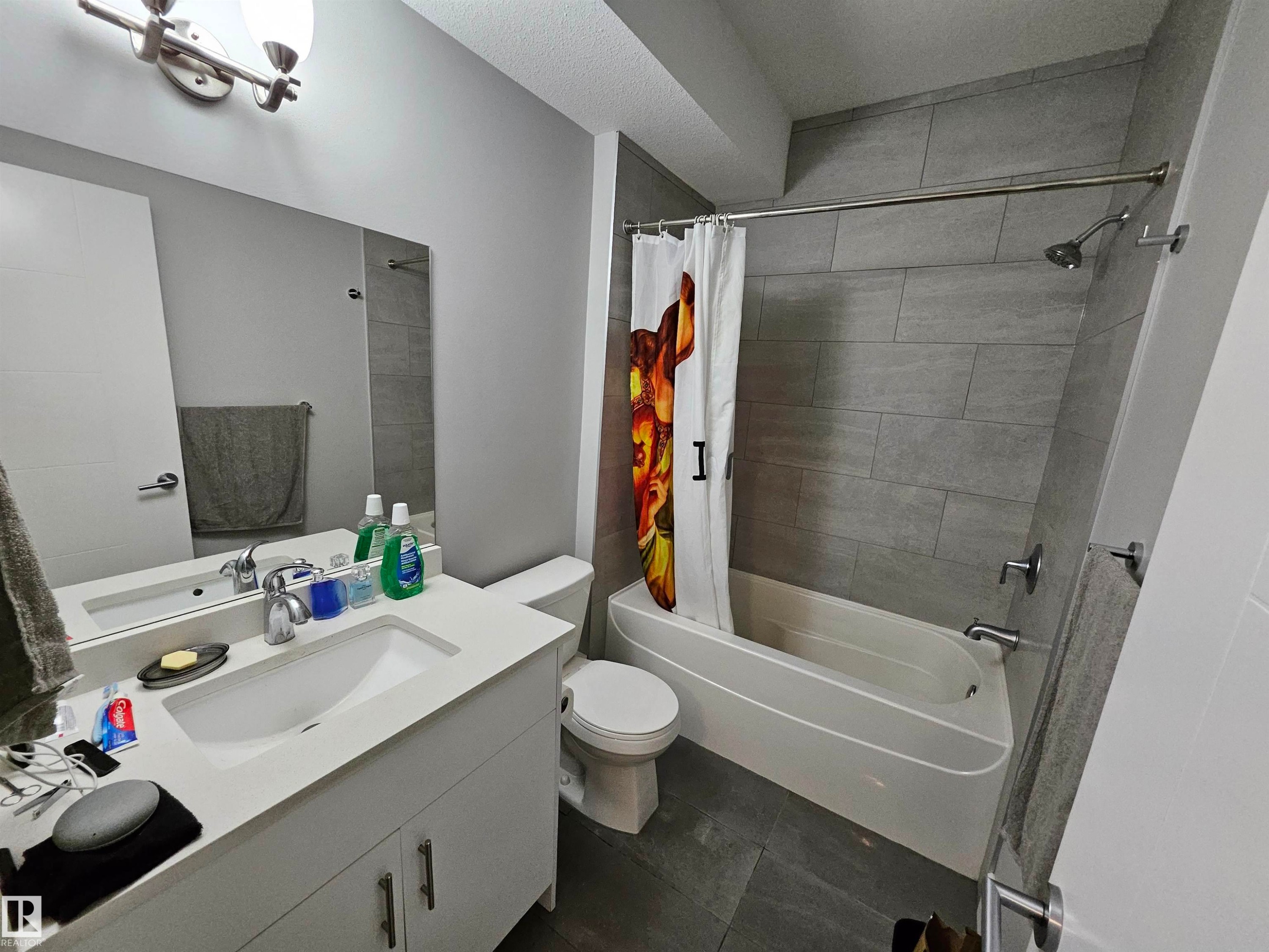 Bathroom featuring a white vanity with integrated sink, a large mirror, and a wall-mounted light fixture - 9311 66 Avenue Nw, Edmonton, AB - Indoor Photo Showing Bathroom