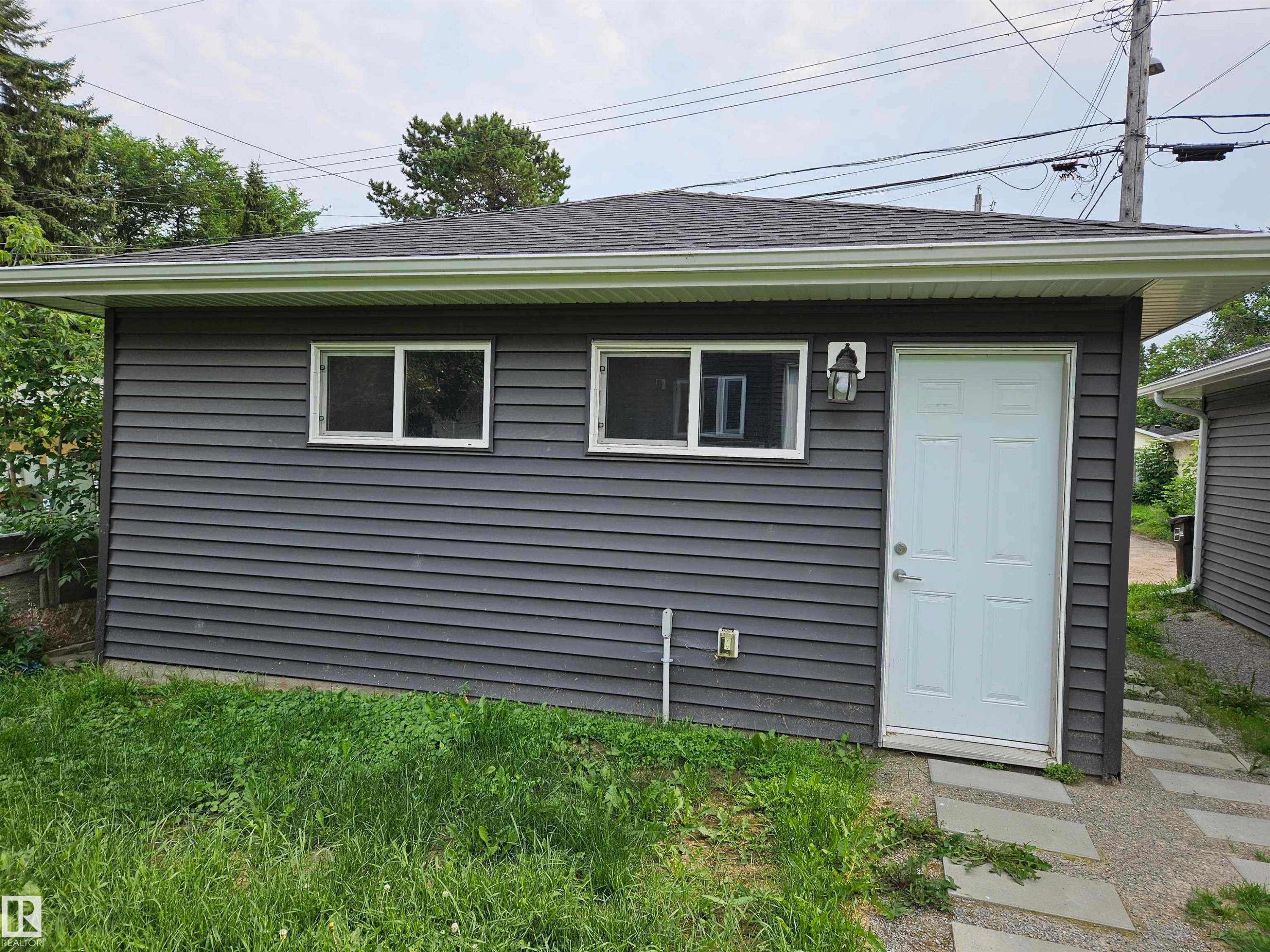 Detached structure with dark gray horizontal siding, a white panel door, and two white-framed windows - 9311 66 Avenue Nw, Edmonton, AB - Outdoor