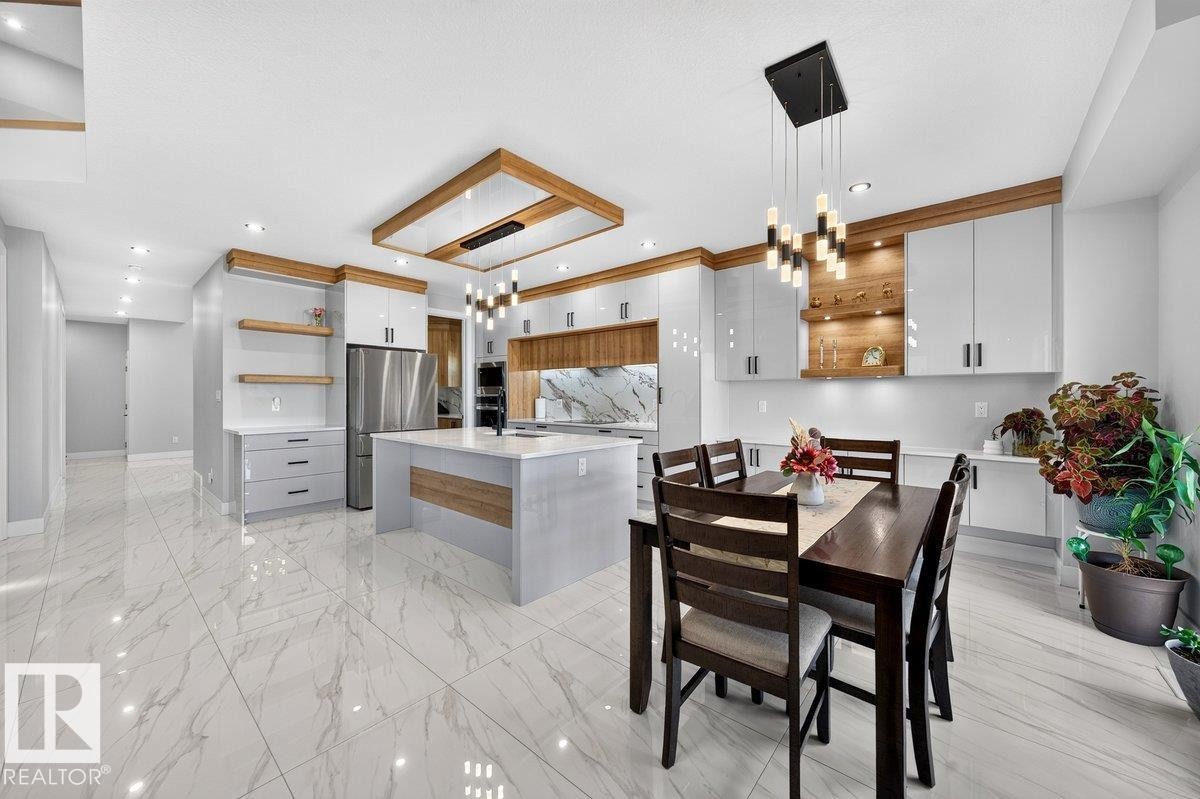 Open-concept kitchen and dining area featuring large-format tile flooring, a central island with integrated seating, stainless steel appliances, and a wood-accented ceiling feature with recessed lighting - 6001 19 Street, Nisku, AB - Indoor