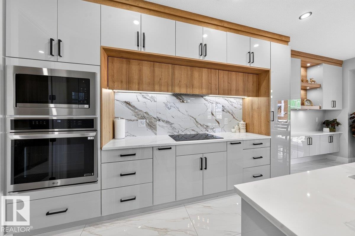 Modern kitchen featuring white high-gloss cabinetry with black hardware, integrated stainless steel appliances, a white patterned backsplash, and wood-finish accents - 6001 19 Street, Nisku, AB - Indoor Photo Showing Kitchen