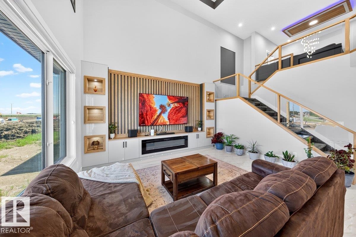 Spacious living area featuring a double-height ceiling, large windows, wood-finish accent wall with integrated shelving, built-in media console with fireplace, and a contemporary staircase with glass railing - 6001 19 Street, Nisku, AB - Indoor Photo Showing Living Room