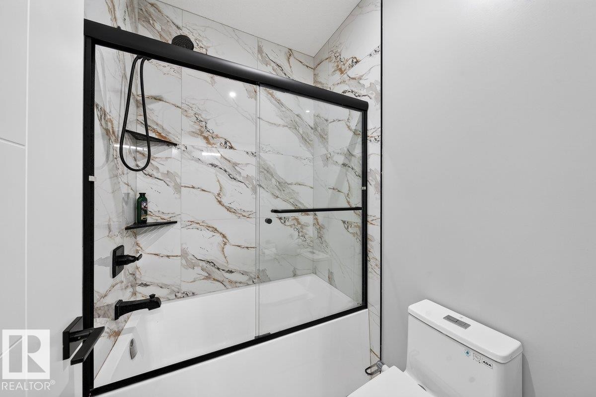 Bathtub-shower combination featuring a frameless glass enclosure with black trim, and marble-patterned wall tiles - 6001 19 Street, Nisku, AB - Indoor Photo Showing Bathroom