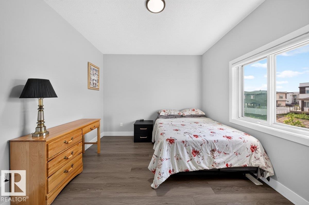Bedroom featuring light gray walls, wood-finish flooring, a contemporary ceiling light fixture, and a large window with white trim - 6001 19 Street, Nisku, AB - Indoor Photo Showing Bedroom
