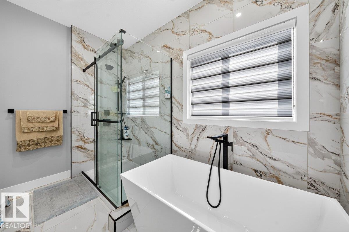 Contemporary bathroom featuring a freestanding soaking tub with a floor-mounted matte black faucet, a glass-enclosed shower with black hardware, and large format marble-look wall and floor tiles - 6001 19 Street, Nisku, AB - Indoor