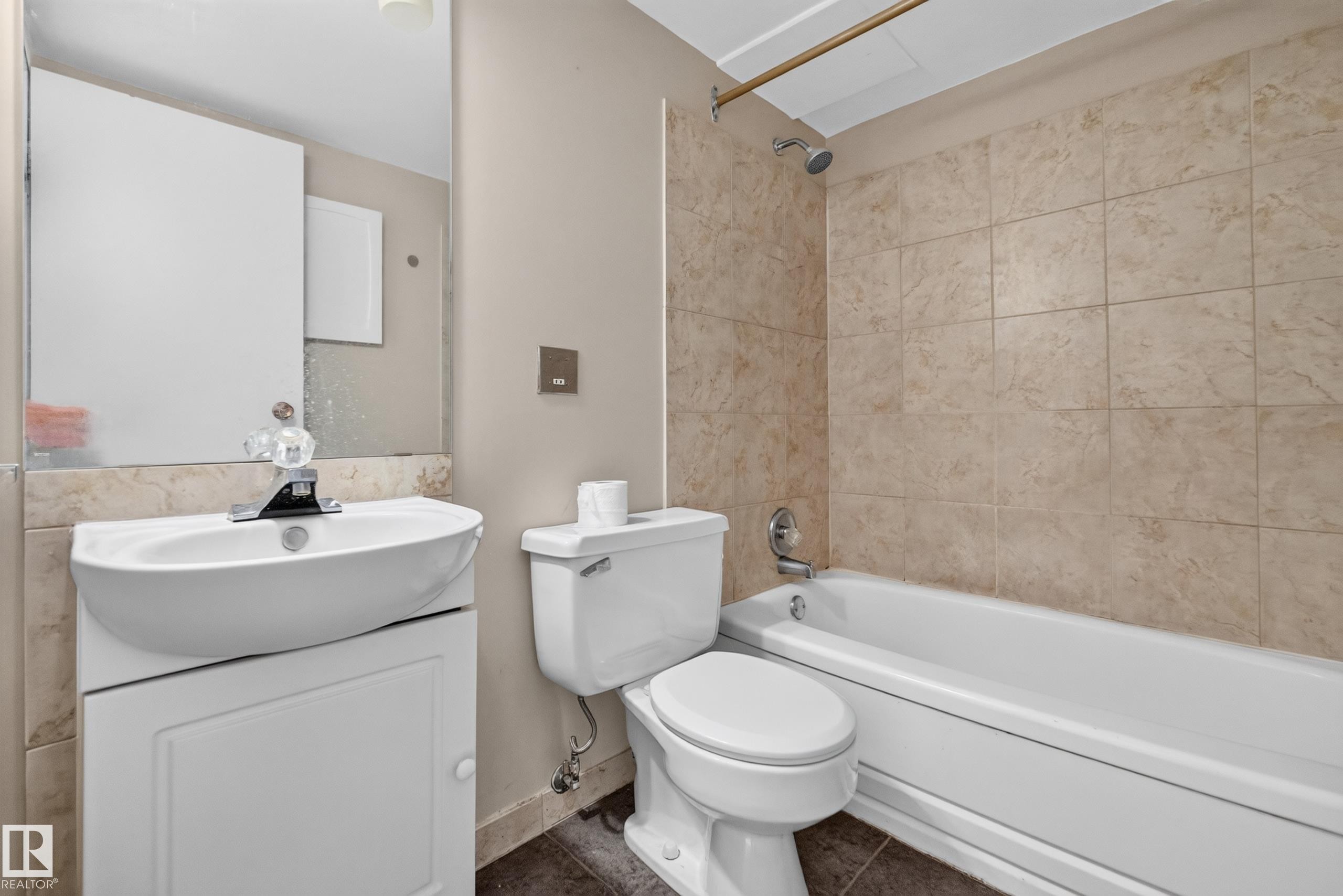 Full bathroom featuring a white porcelain tub with integrated shower, beige tiled surround, and a coordinating vanity with a white basin and mirrored medicine cabinet - #1804 10883 Saskatchewan Dr Nw, Edmonton, AB - Indoor Photo Showing Bathroom