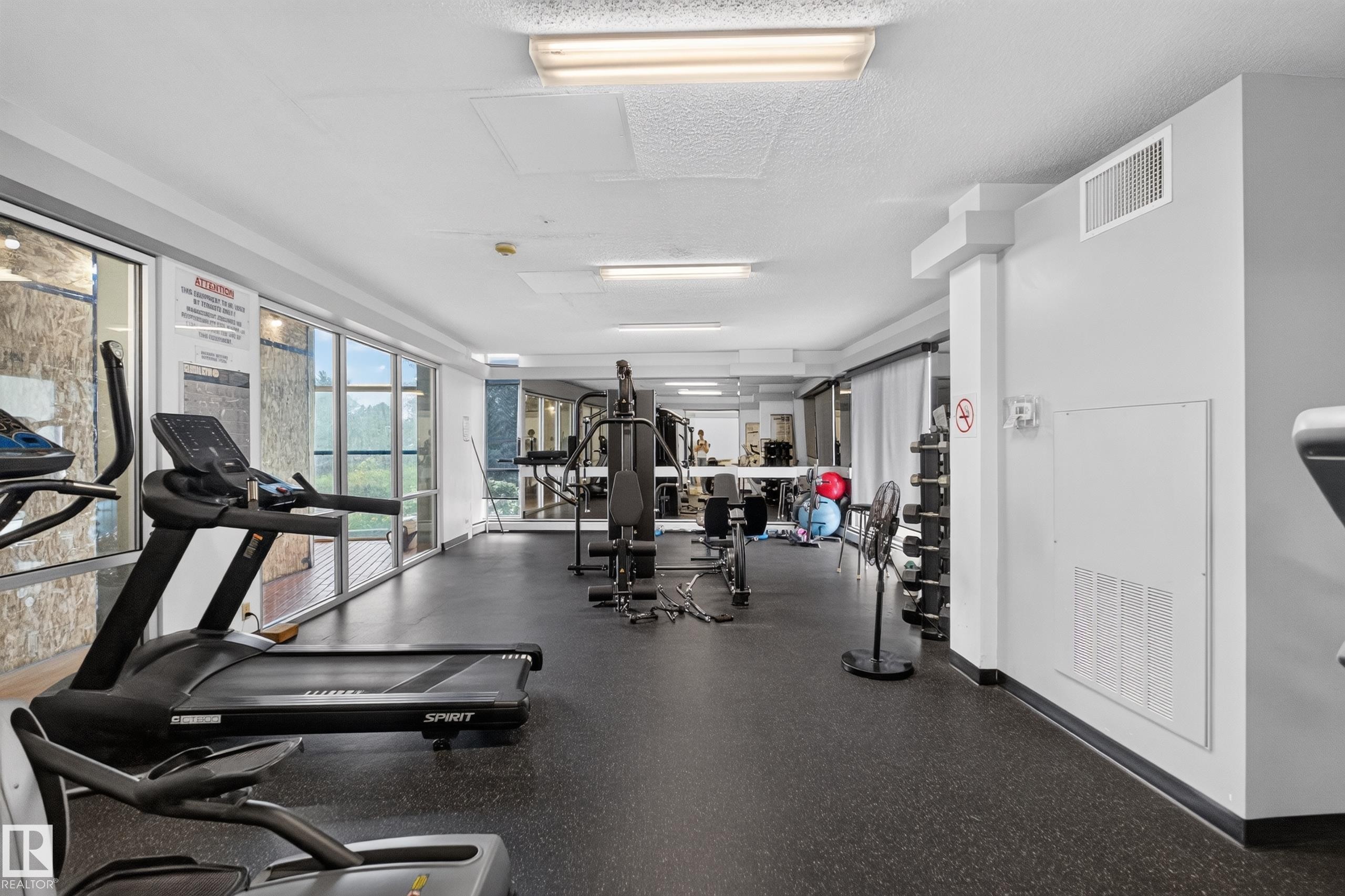 Fitness center featuring extensive full-height windows, durable black rubber flooring, and bright overhead fluorescent lighting - #1804 10883 Saskatchewan Dr Nw, Edmonton, AB - Indoor Photo Showing Gym Room