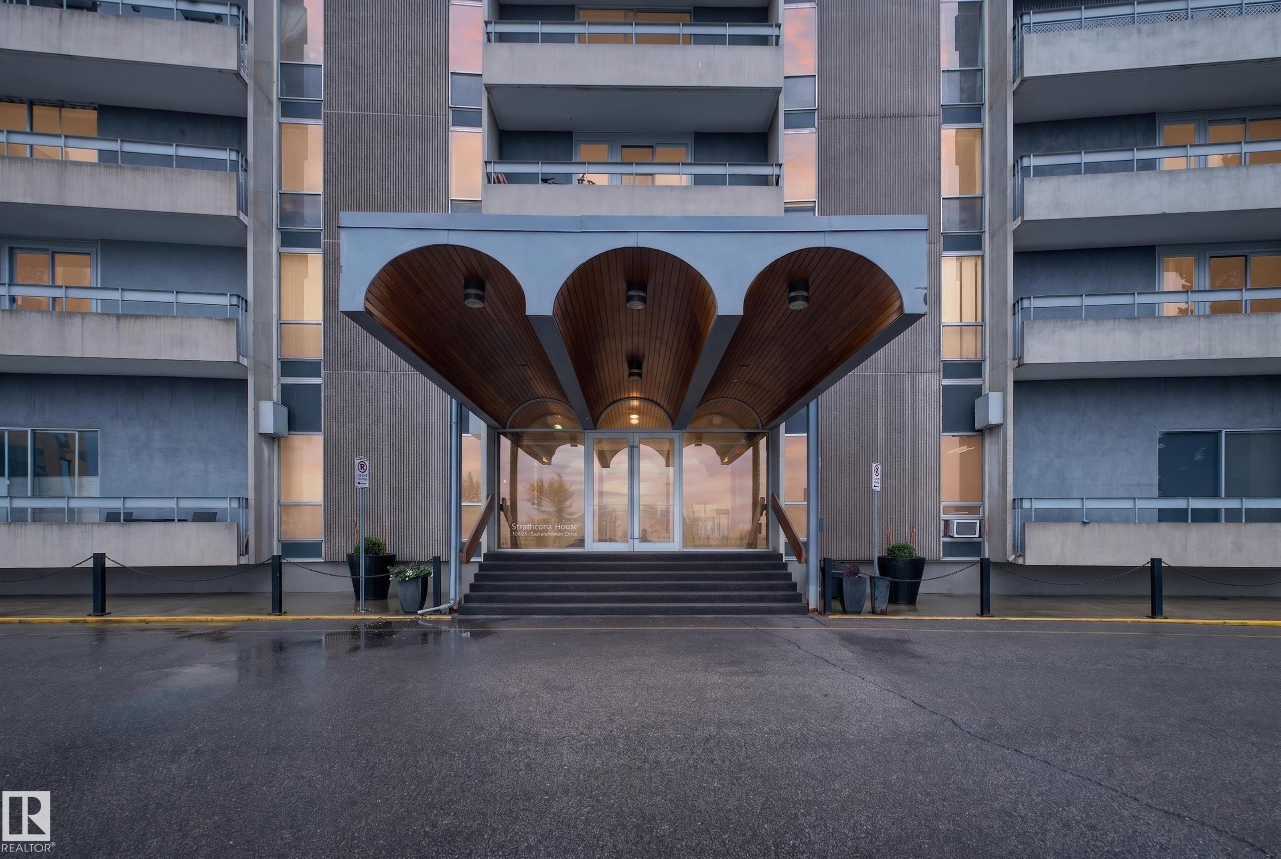 Multi-story building entrance with a covered portico featuring three arched wood-paneled ceilings and integrated lighting - #1804 10883 Saskatchewan Dr Nw, Edmonton, AB - Outdoor With Balcony