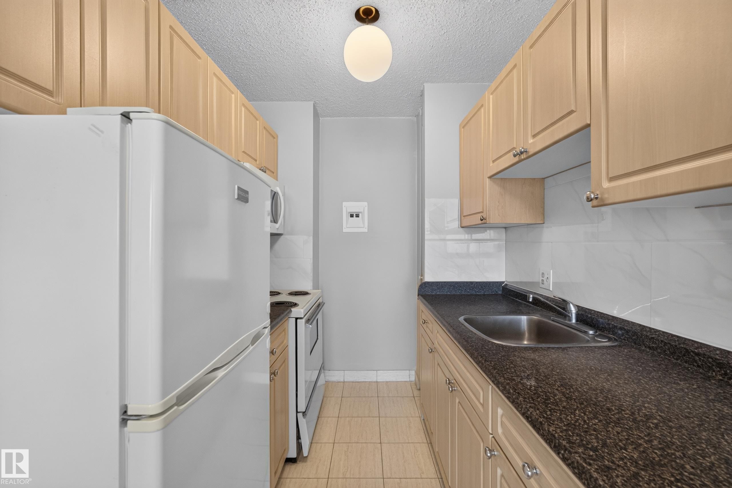 Galley kitchen featuring light wood-finish cabinetry, a white tile backsplash, and dark speckled countertops - #1508 10883 Saskatchewan Dr Nw Nw, Edmonton, AB - Indoor Photo Showing Kitchen