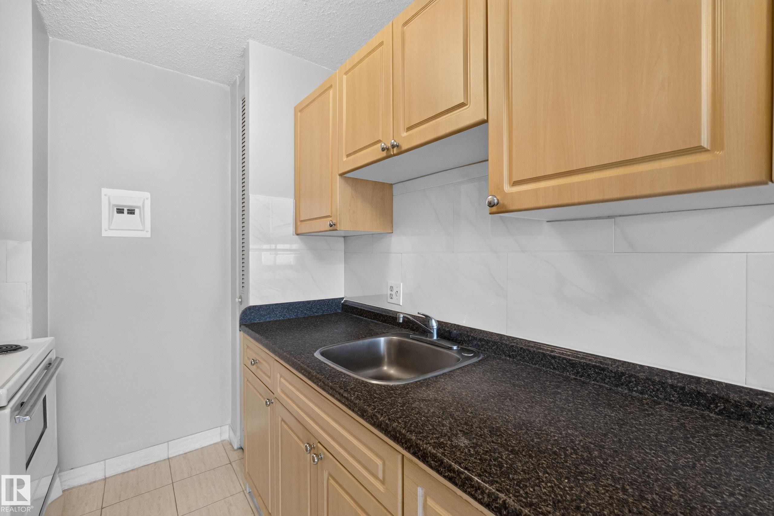 Kitchen featuring light wood cabinetry, dark speckled countertops, and a stainless steel sink - #1508 10883 Saskatchewan Dr Nw Nw, Edmonton, AB - Indoor Photo Showing Kitchen