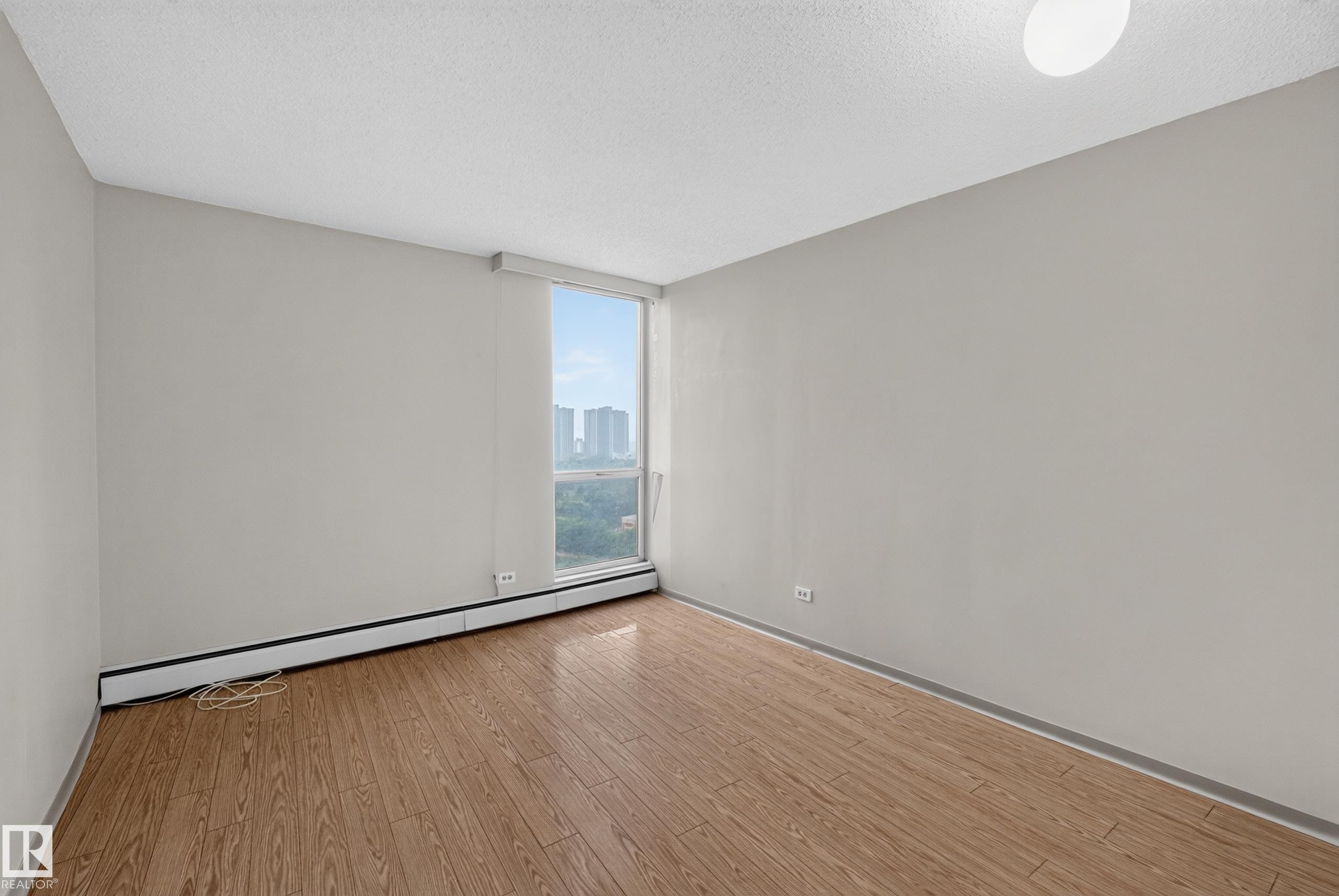 Bright interior space featuring a large window, wood-finish flooring, light gray wall tones, and a ceiling-mounted light fixture - #1508 10883 Saskatchewan Dr Nw Nw, Edmonton, AB - Indoor Photo Showing Other Room