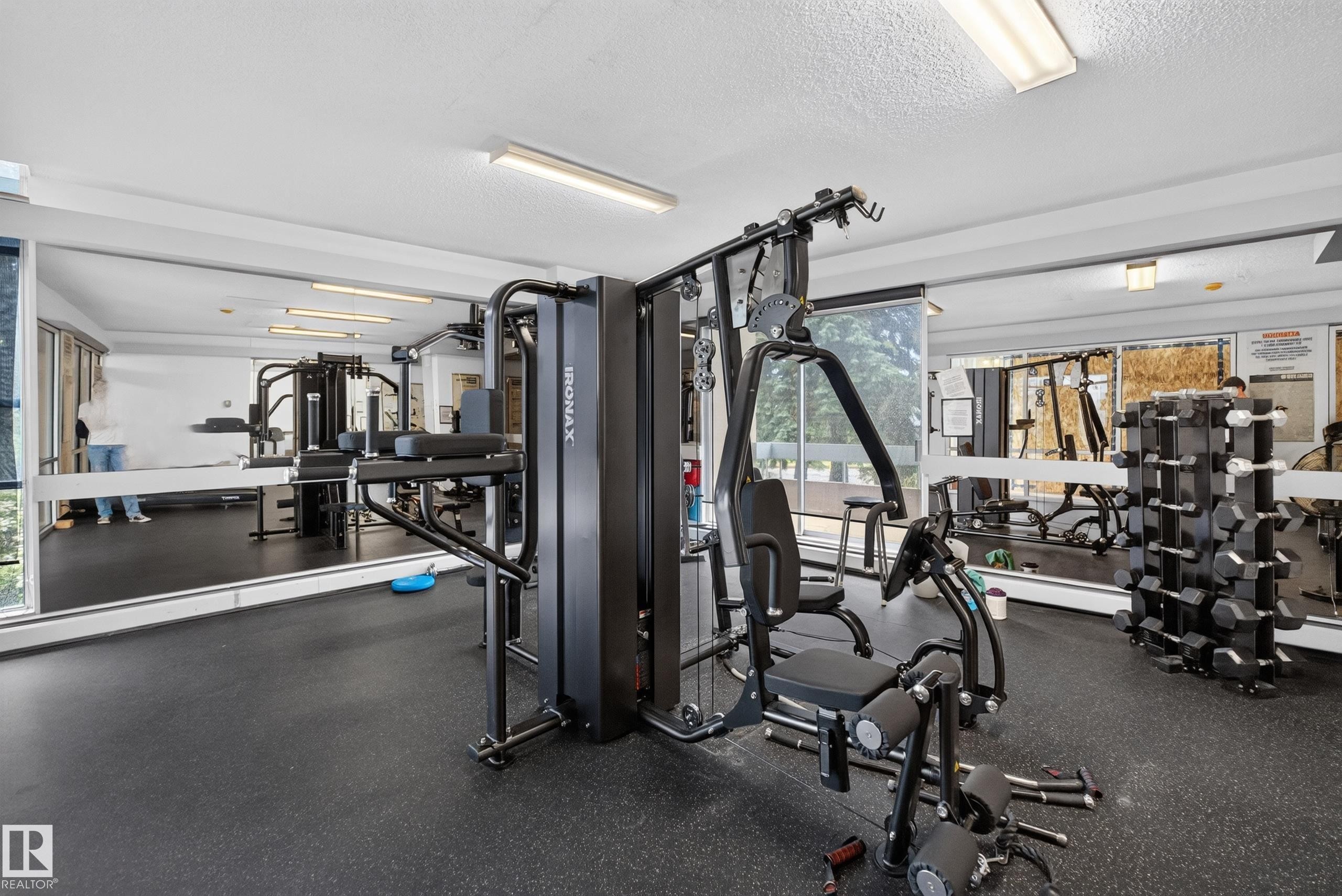 Dedicated fitness area featuring a multi-station home gym, full wall mirrors, rubberized flooring, and extensive window-line - #1508 10883 Saskatchewan Dr Nw Nw, Edmonton, AB - Indoor Photo Showing Gym Room