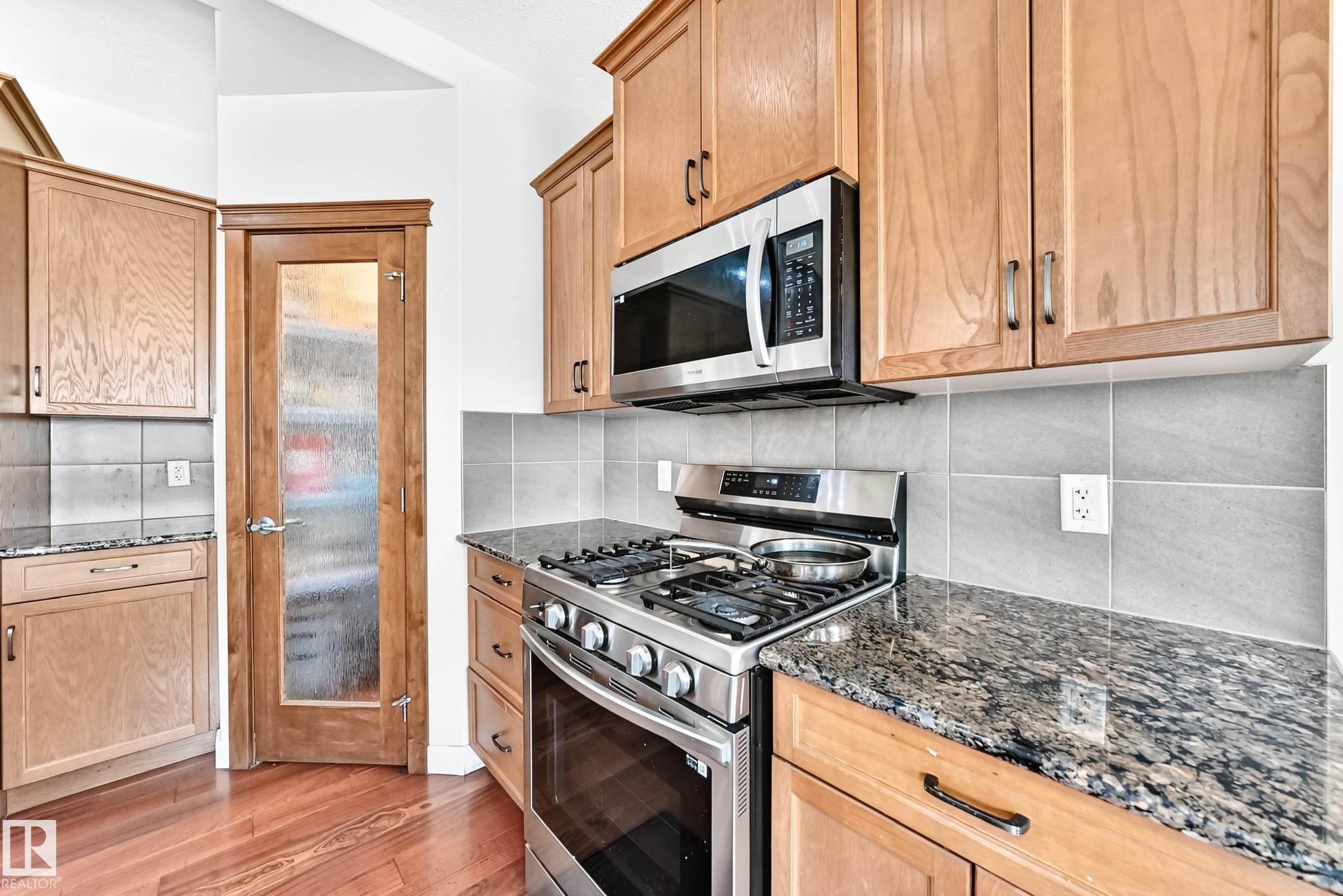 Kitchen featuring light wood cabinetry, granite countertops, stainless steel appliances, a tile backsplash, and wood-finish flooring - 2923 16 Street Nw, Edmonton, AB - Indoor Photo Showing Kitchen