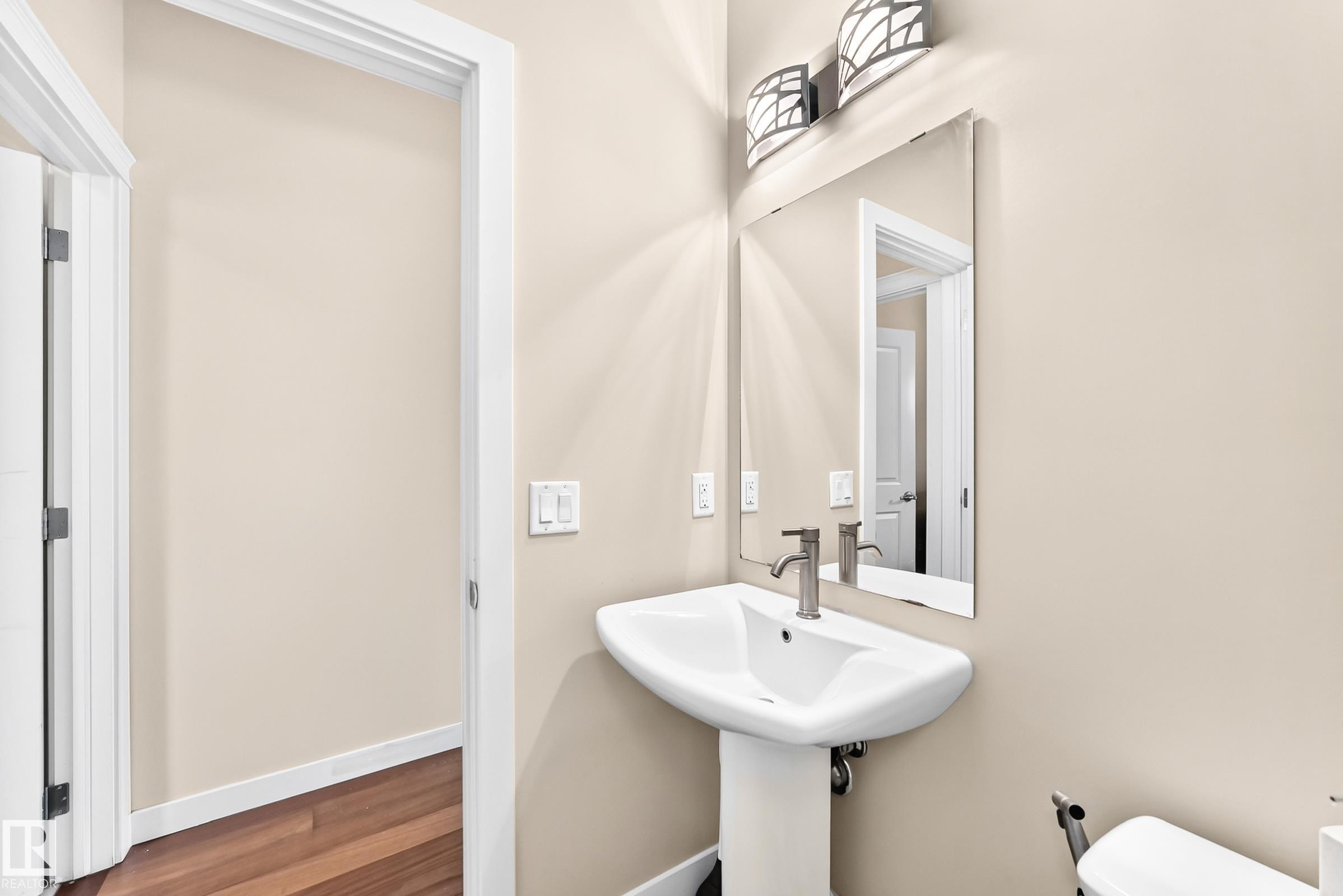 Pedestal sink with a brushed nickel faucet, framed mirror, and decorative wall sconces - 2923 16 Street Nw, Edmonton, AB - Indoor Photo Showing Bathroom
