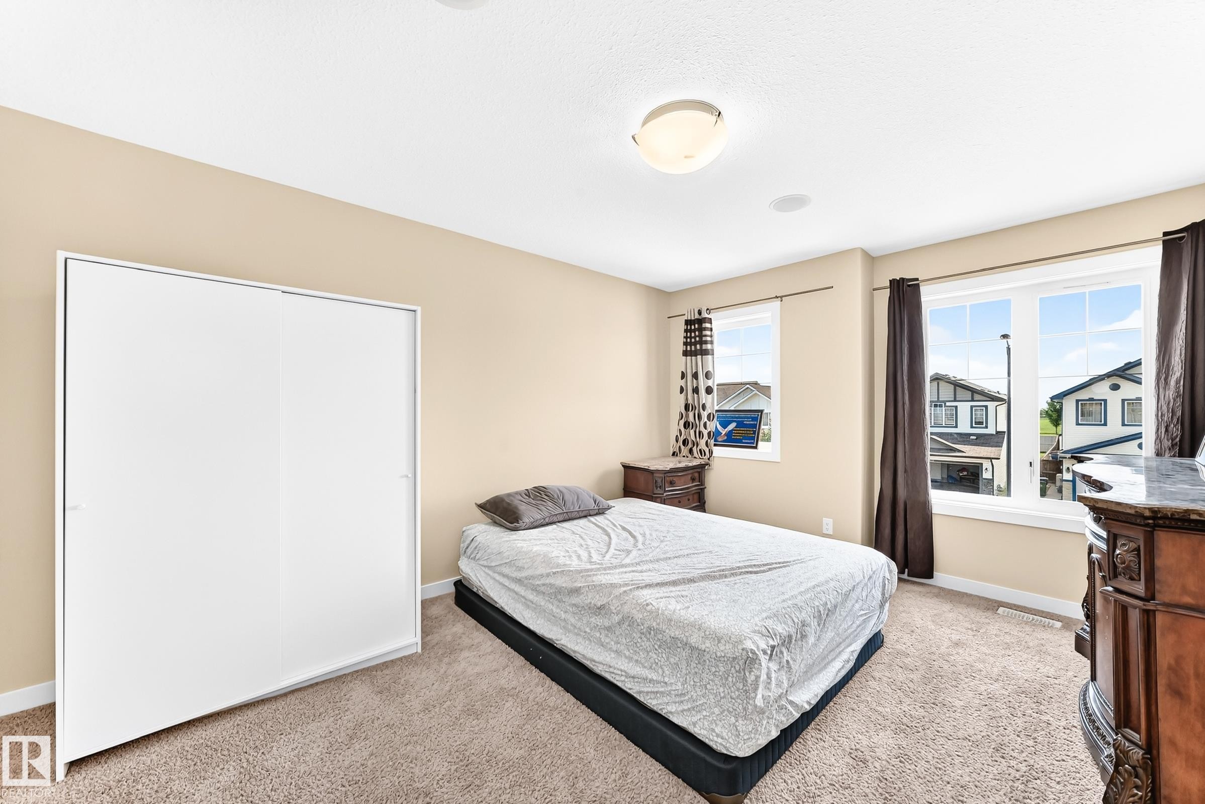 Neutral-toned room featuring a ceiling-mounted light fixture, two windows with white trim, and light brown carpeting - 2923 16 Street Nw, Edmonton, AB - Indoor Photo Showing Bedroom
