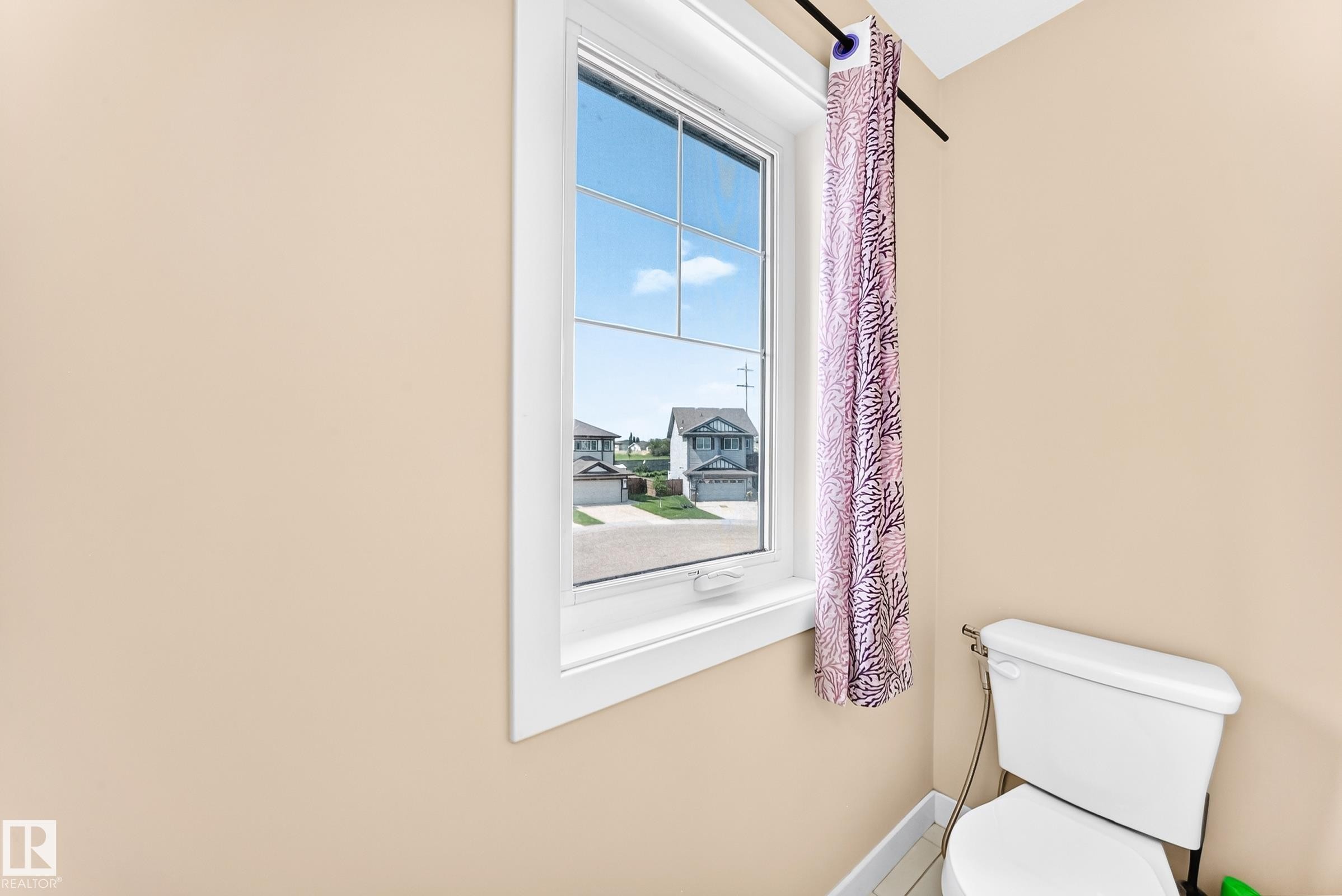 Vertical window with white trim, featuring a white toilet with visible plumbing, and light-colored walls - 2923 16 Street Nw, Edmonton, AB - Indoor Photo Showing Bathroom
