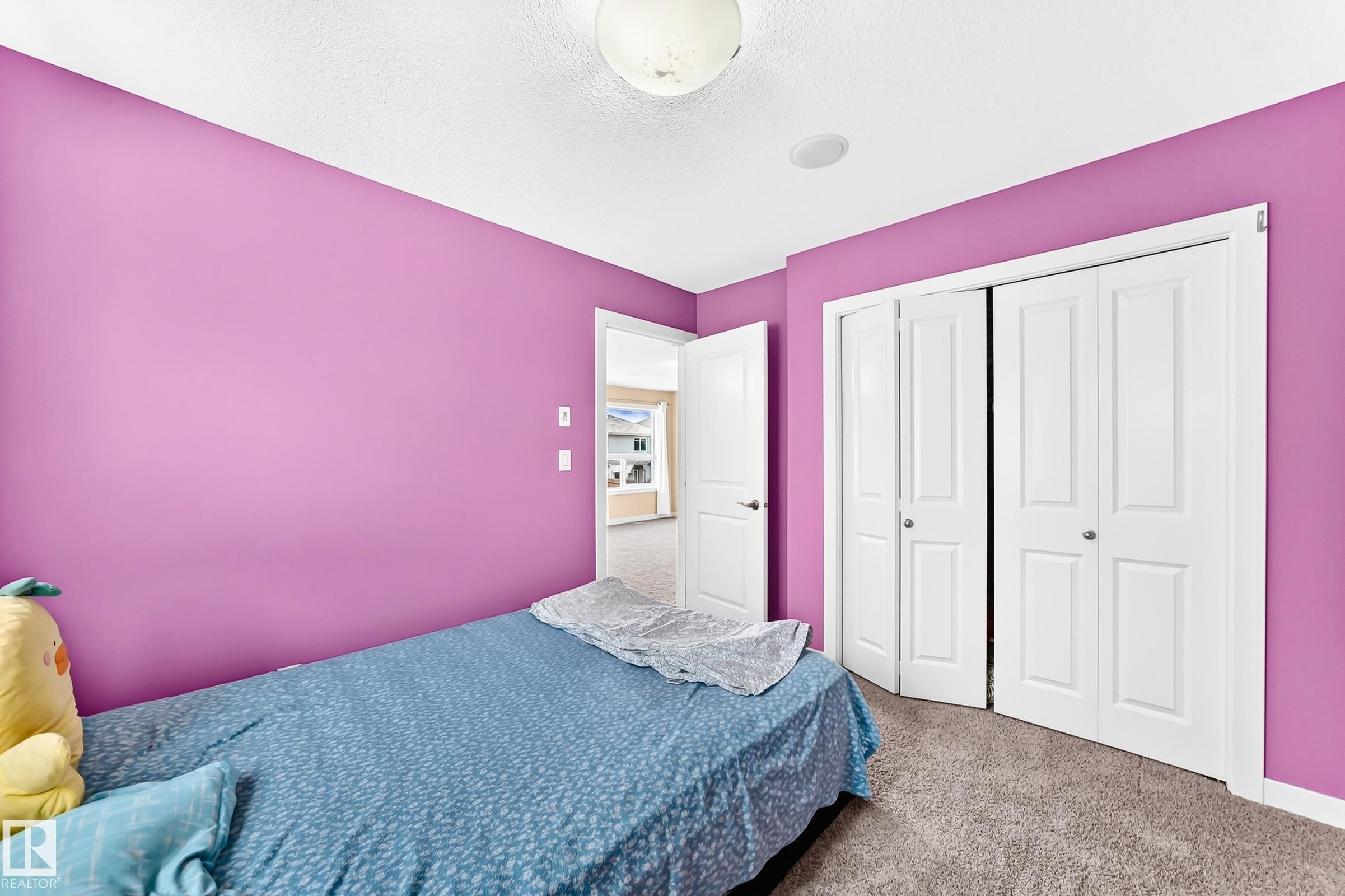 Bedroom featuring bold wall color, carpet flooring, a ceiling-mounted light fixture, built-in closet with bi-fold doors, and a white interior door - 2923 16 Street Nw, Edmonton, AB - Indoor Photo Showing Bedroom